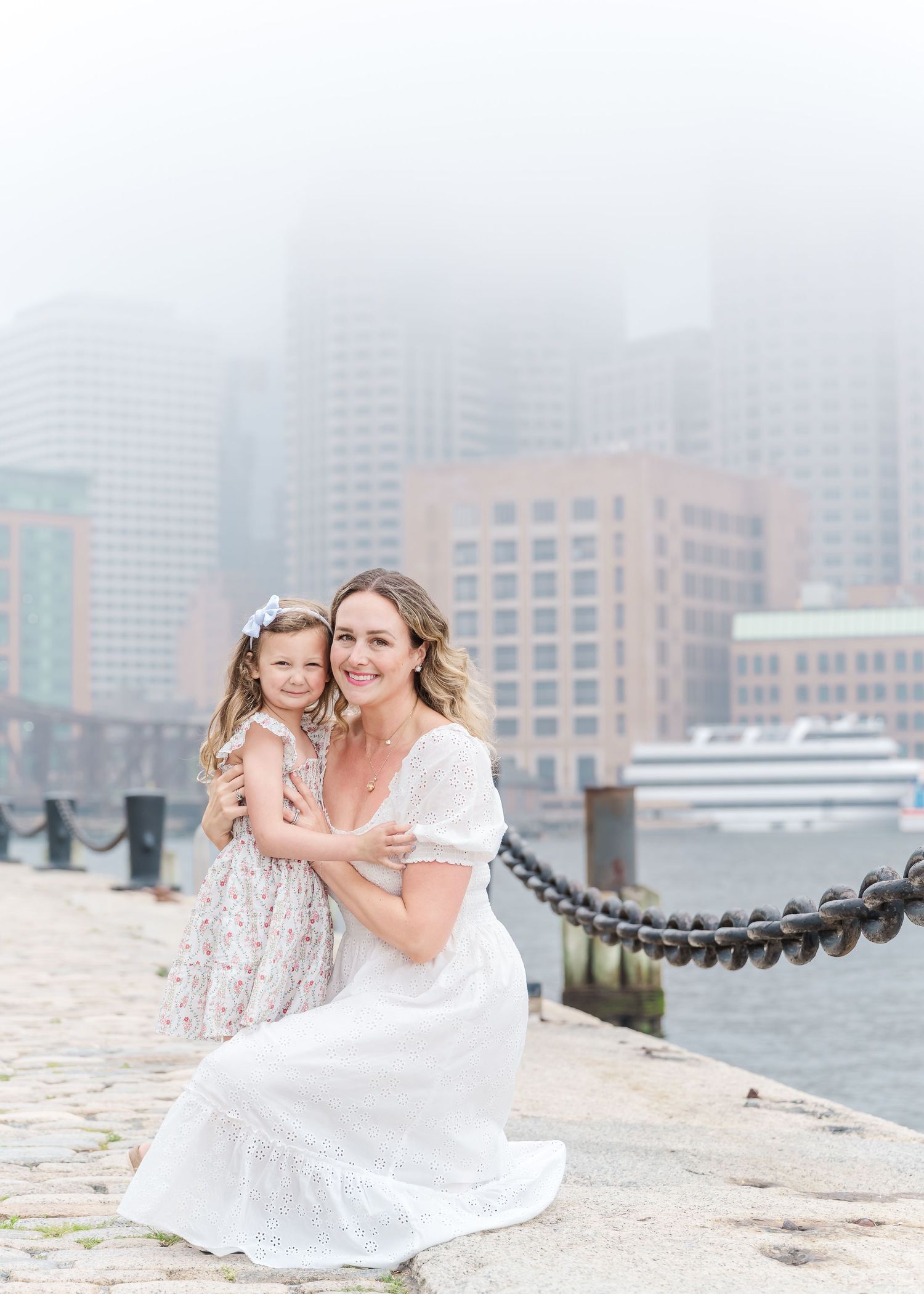 Sweet embraces shared on a waterfront with misty urban backdrop and boats in the harbor.