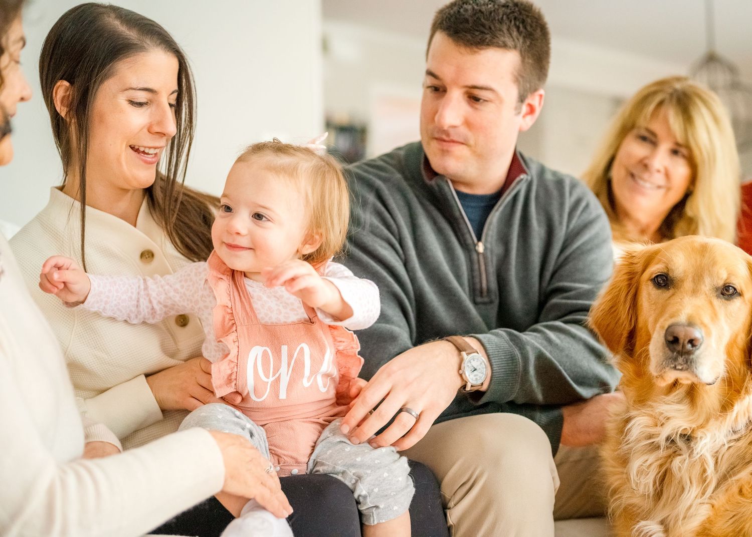 Family gathering on couch with golden retriever dog in living room setting.