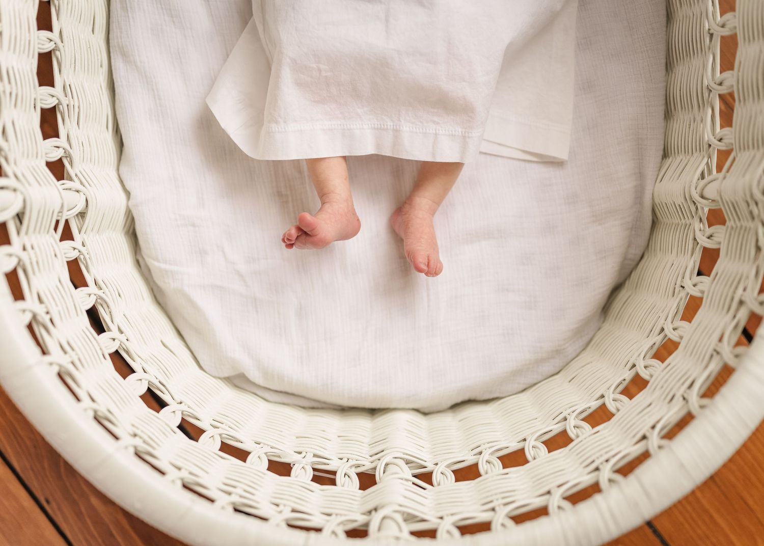 Tiny baby feet peek out from white linen in a woven bassinet.