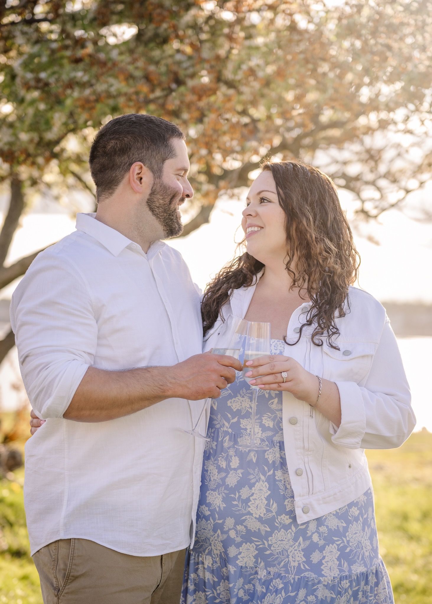 A couple shares champagne and laughter under a blooming tree at sunset.