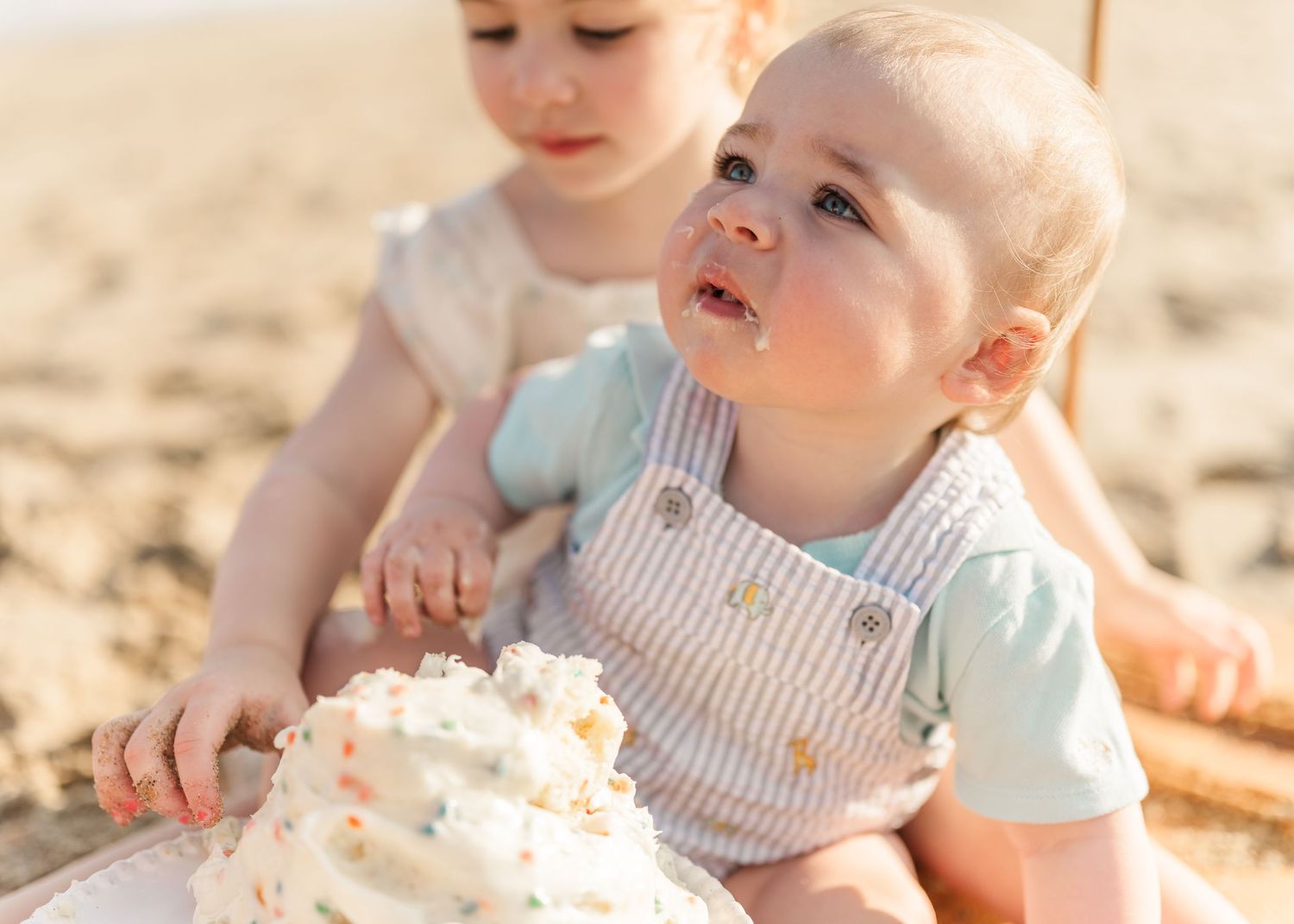 Children sitting on sandy ground playing with whipped cream or frosting in warm sunlight.