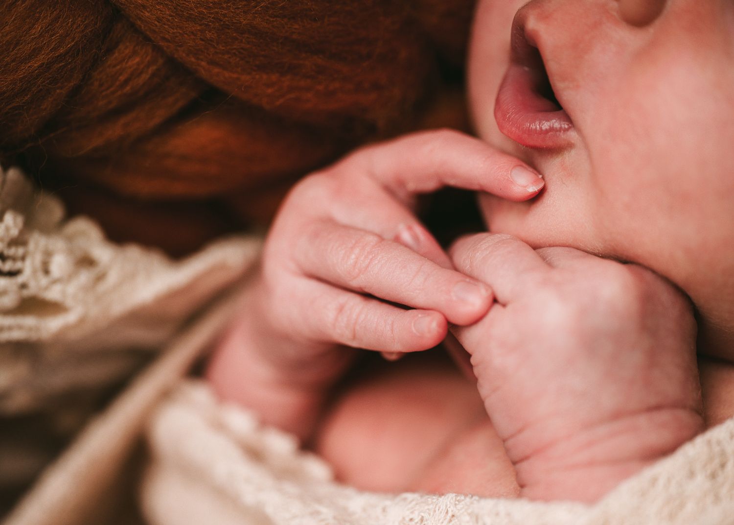 Close-up of baby hands near face in soft natural lighting.