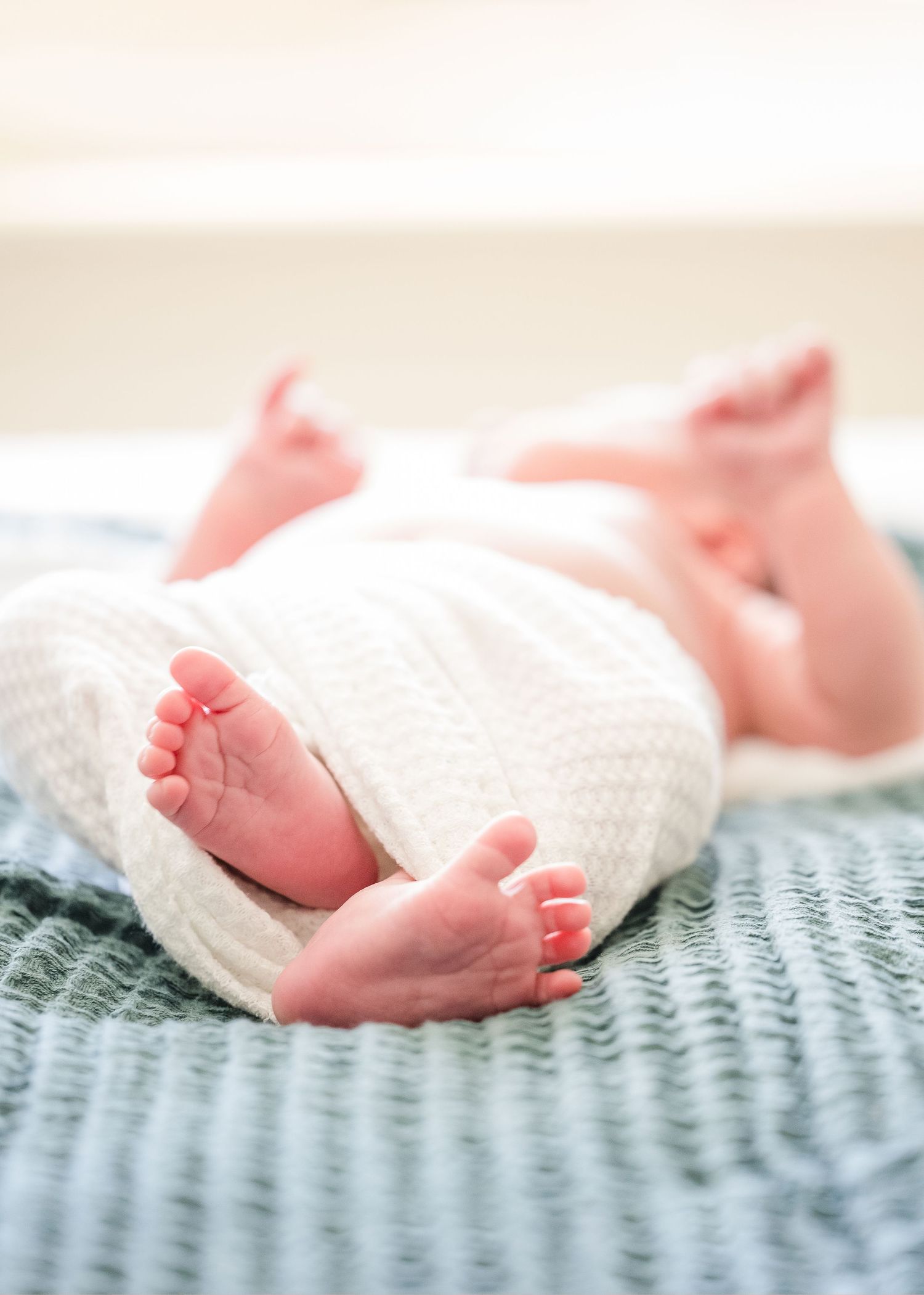 Close up of tiny baby feet wrapped in white knit blanket on blue bedding.