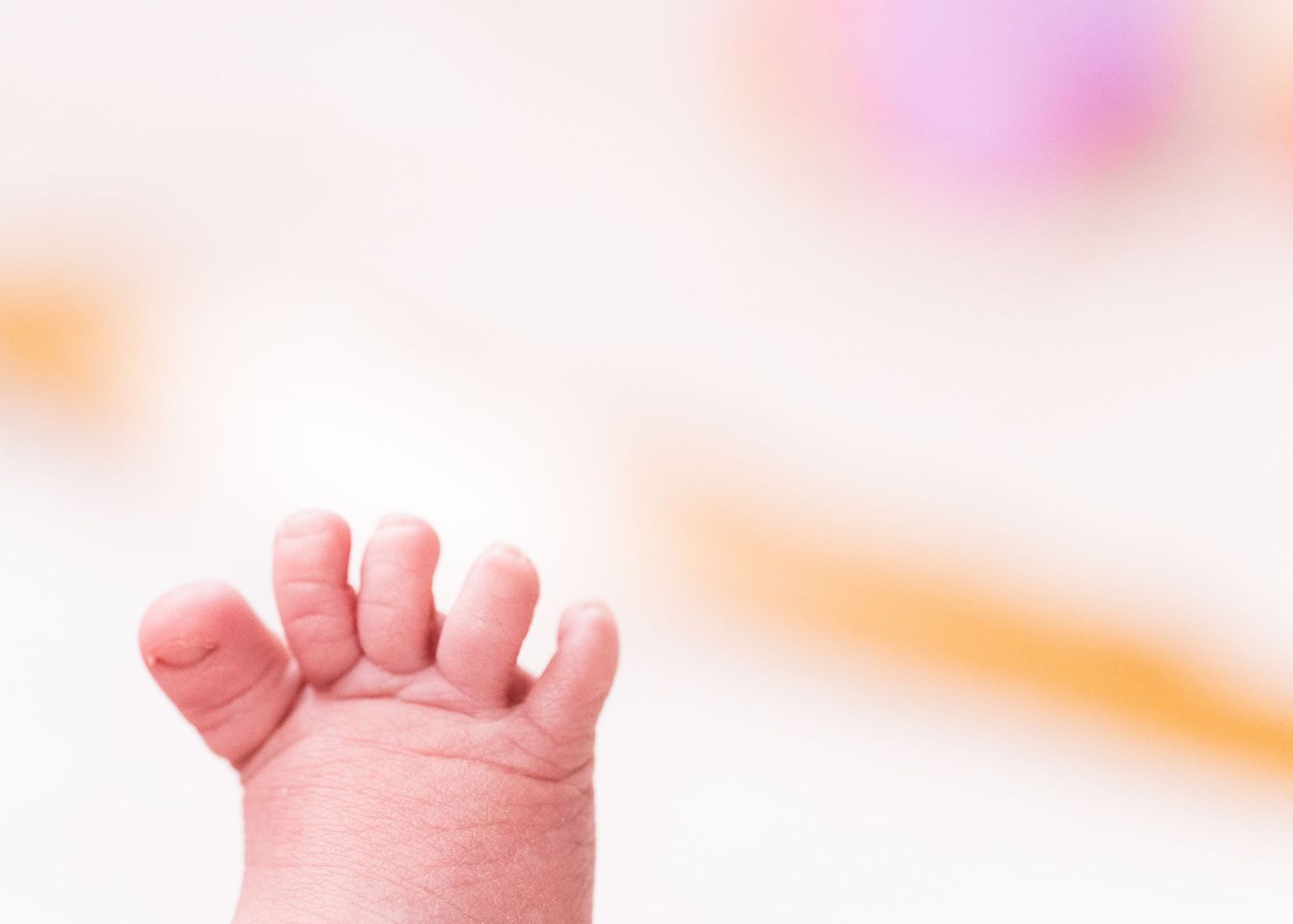 Close-up view of a tiny baby foot with delicate toes against a soft blurred pastel background.