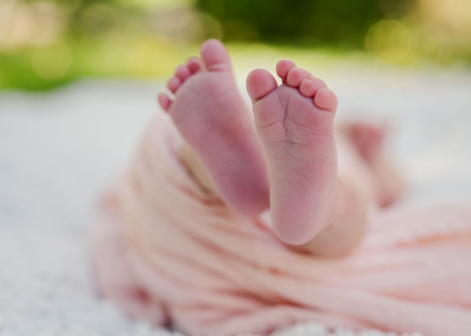 Close-up of tiny newborn baby feet resting on soft pink fabric.