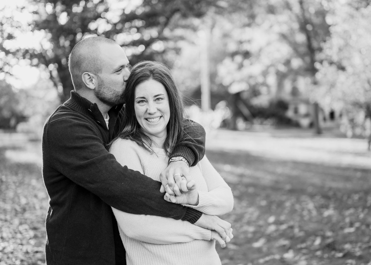 An intimate black and white portrait of a couple embracing outdoors.