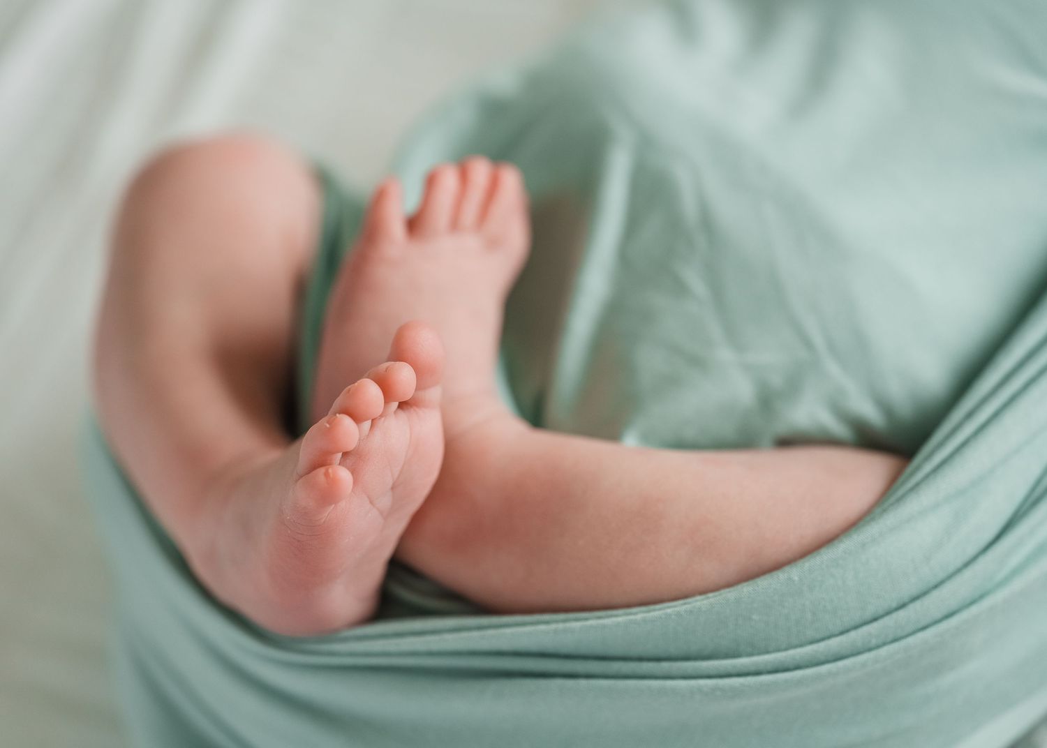 Tiny baby feet peek out from soft mint green blanket in close-up view.