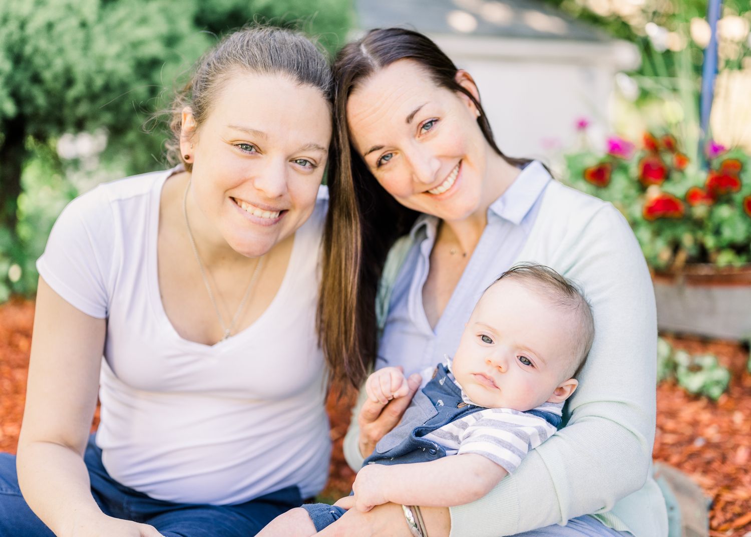 Sunny outdoor family portrait in garden with bright flowers and mulch background.