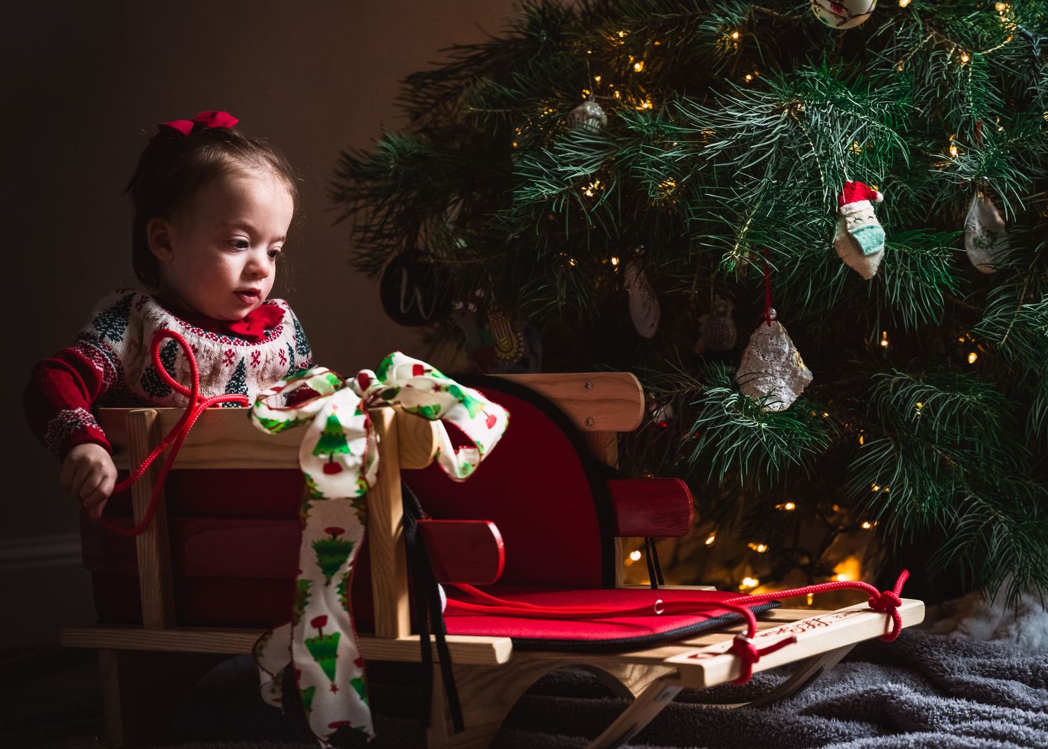 Child in red dress explores Christmas decorations by illuminated tree.