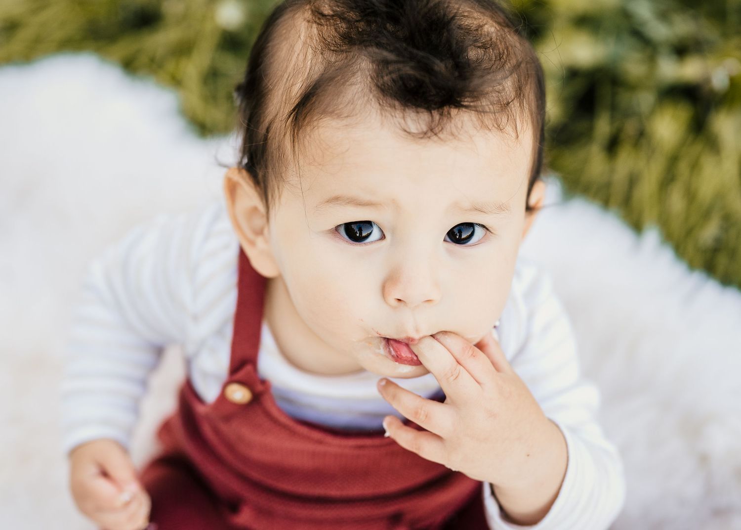Close up of baby in red overalls during first birthday cake smash session.