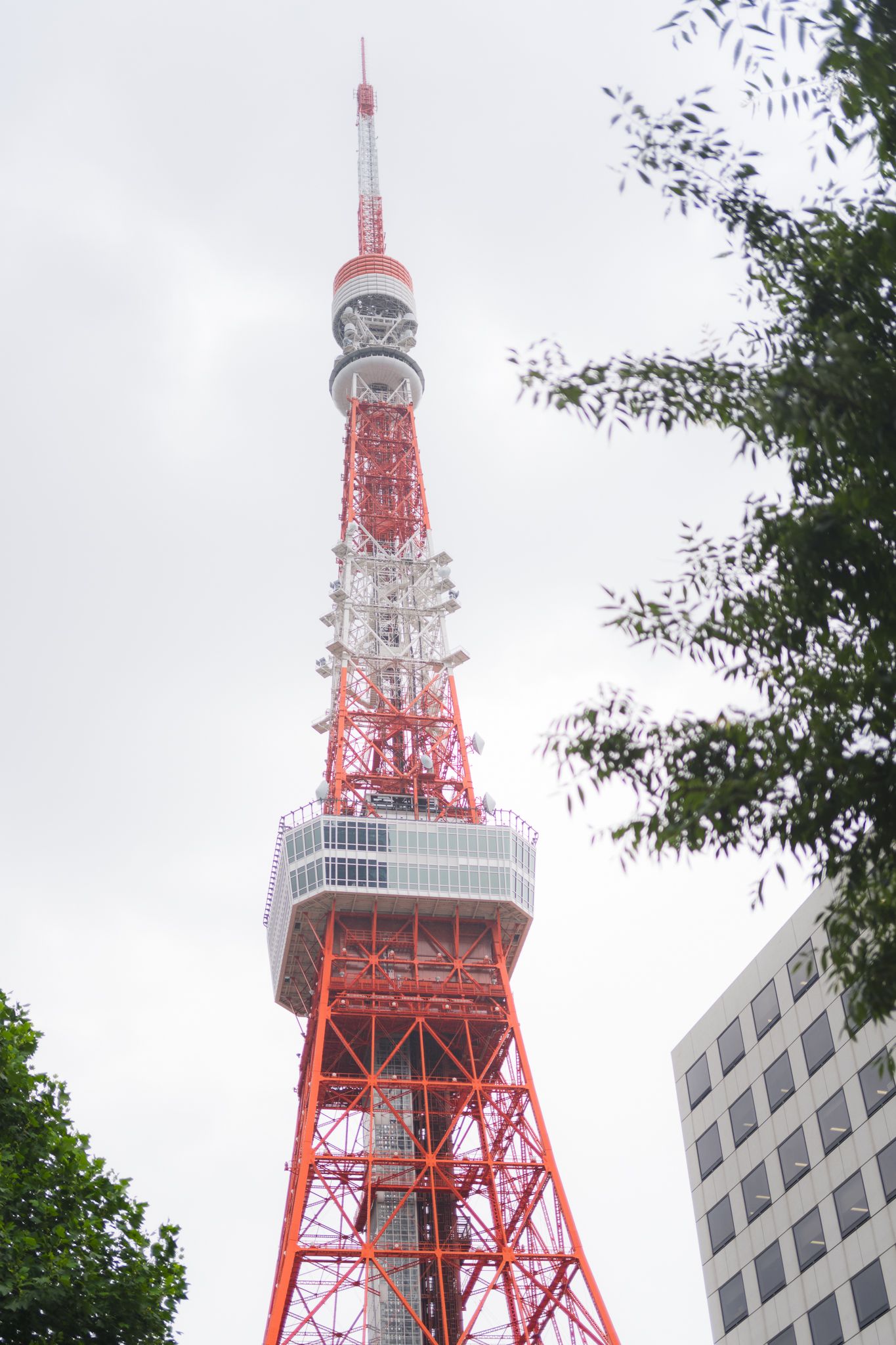 Tokyo Tower stands tall against a cloudy sky with its iconic red and white steel lattice structure.