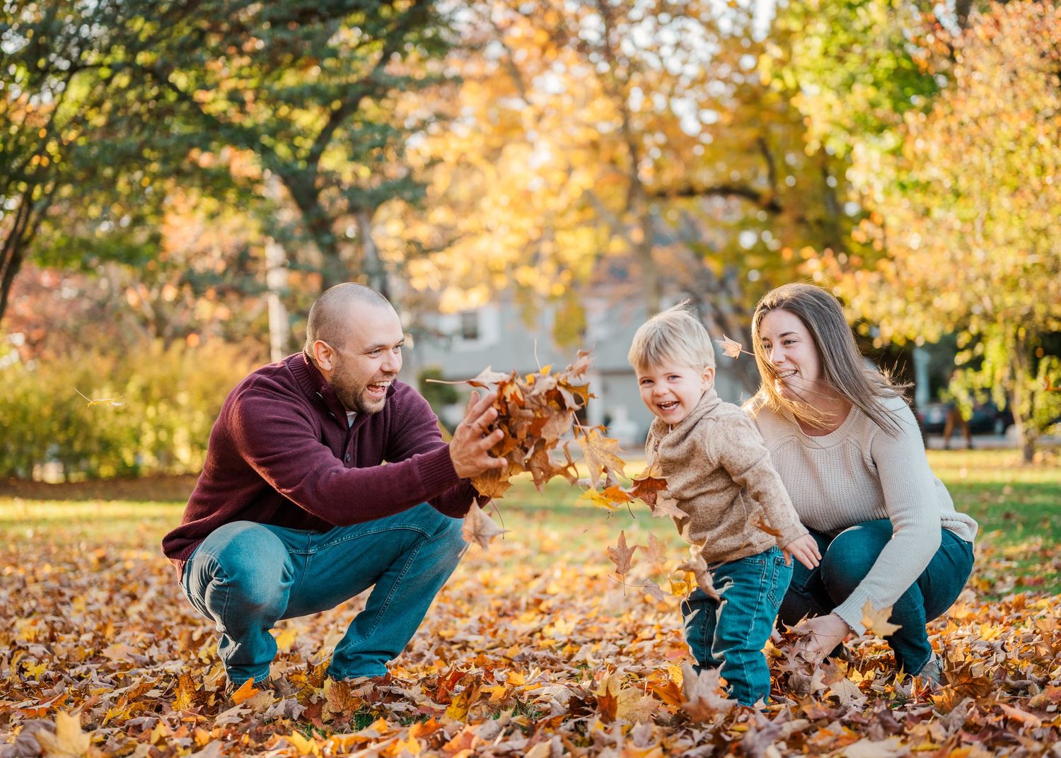 A family plays together in fallen autumn leaves on a sunny day in the park at sunset.