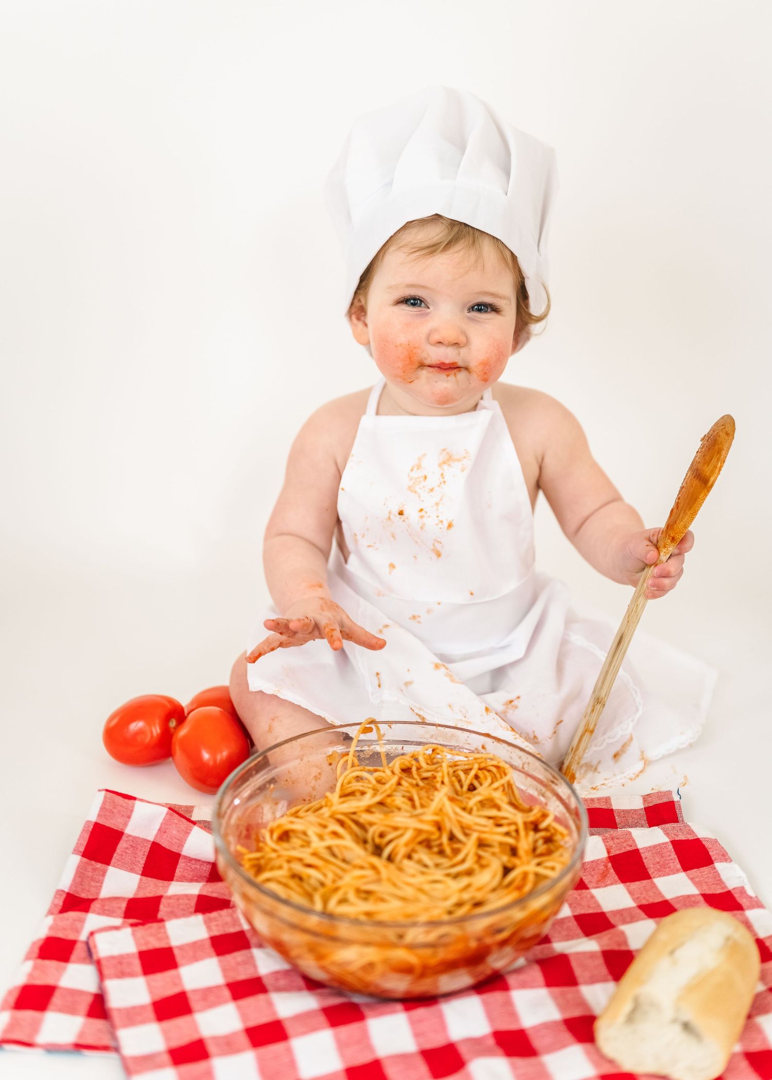 Spaghetti Smash first birthday. A spaghetti dinner setting on a red checkered tablecloth with bread and tomatoes.
