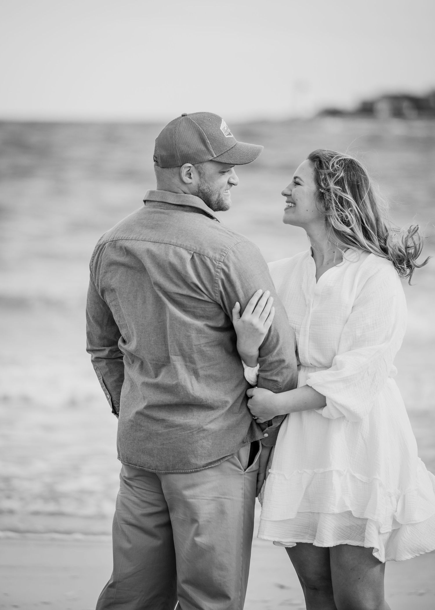 A black and white beach portrait of a couple sharing a romantic moment by the ocean.