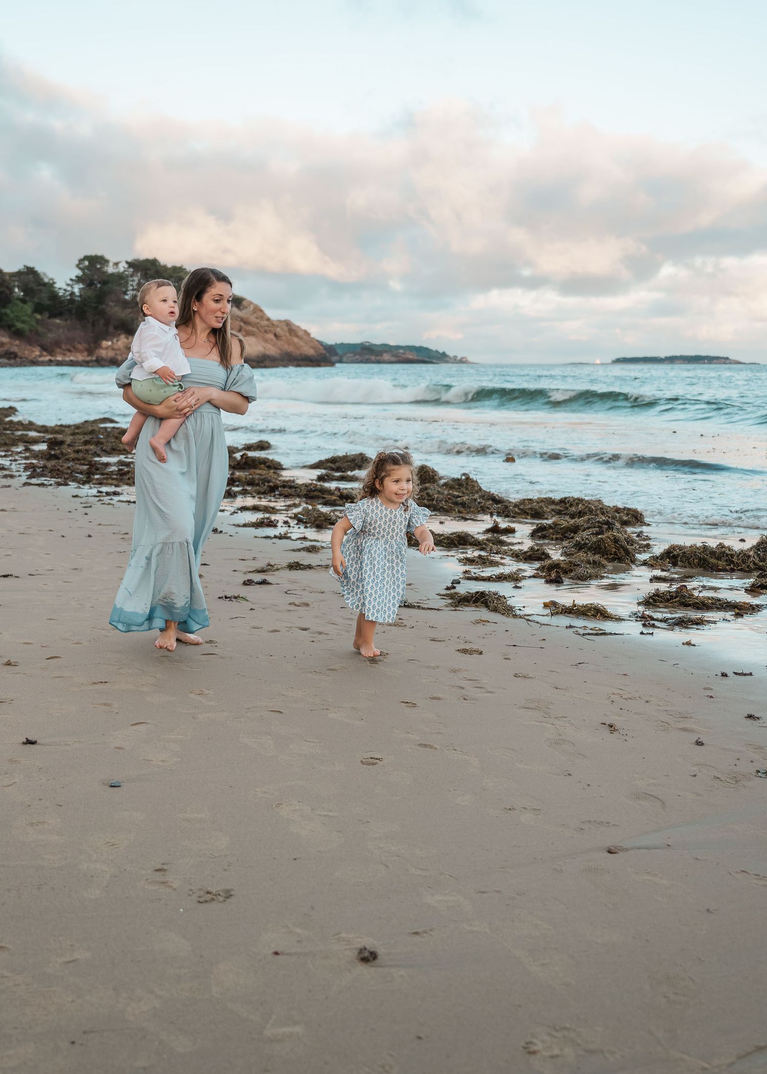 A family walks along a beautiful beach at sunset with waves and rocky cliffs in the background.