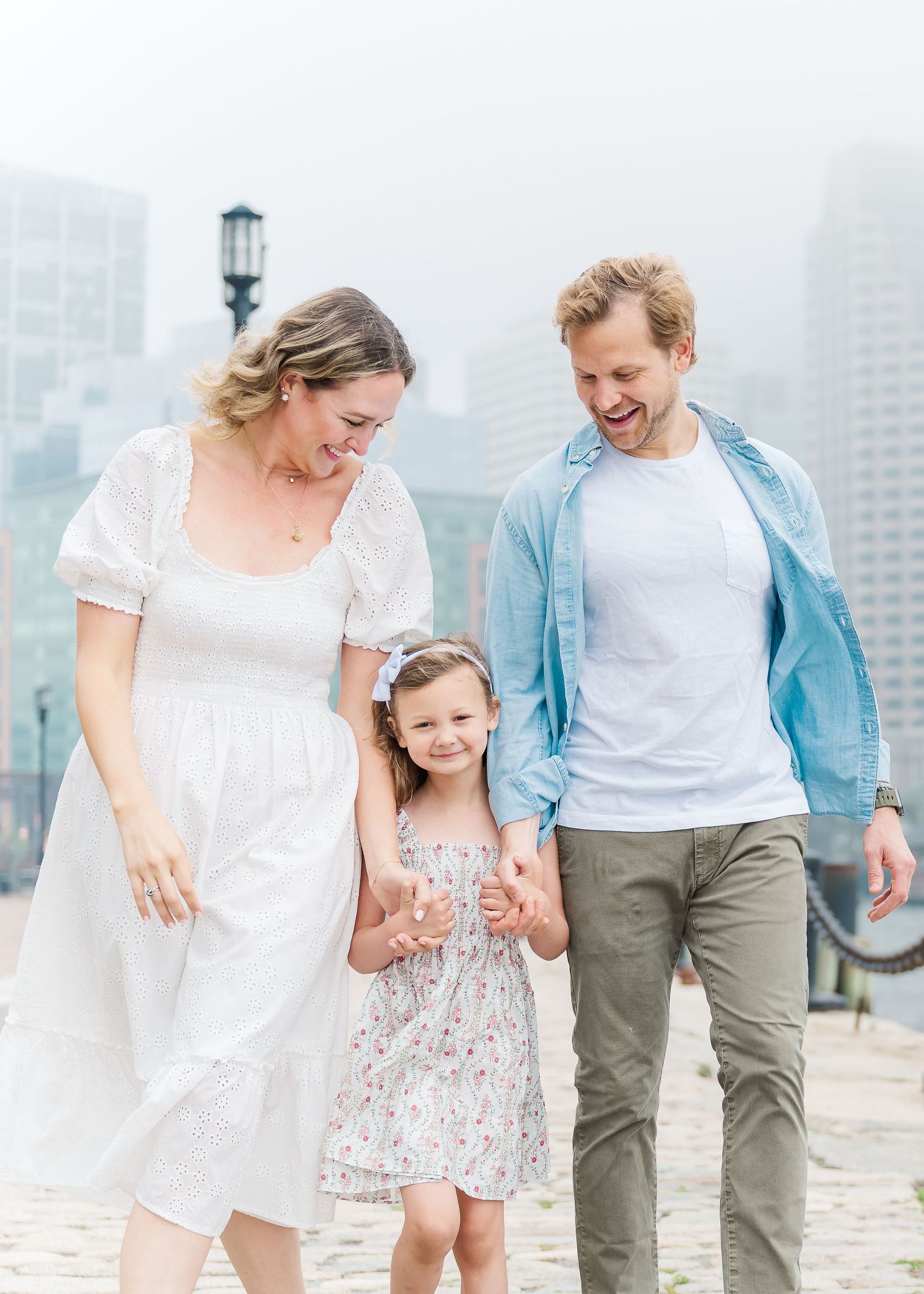 A family shares a joyful moment together on a misty waterfront with city buildings in the background.