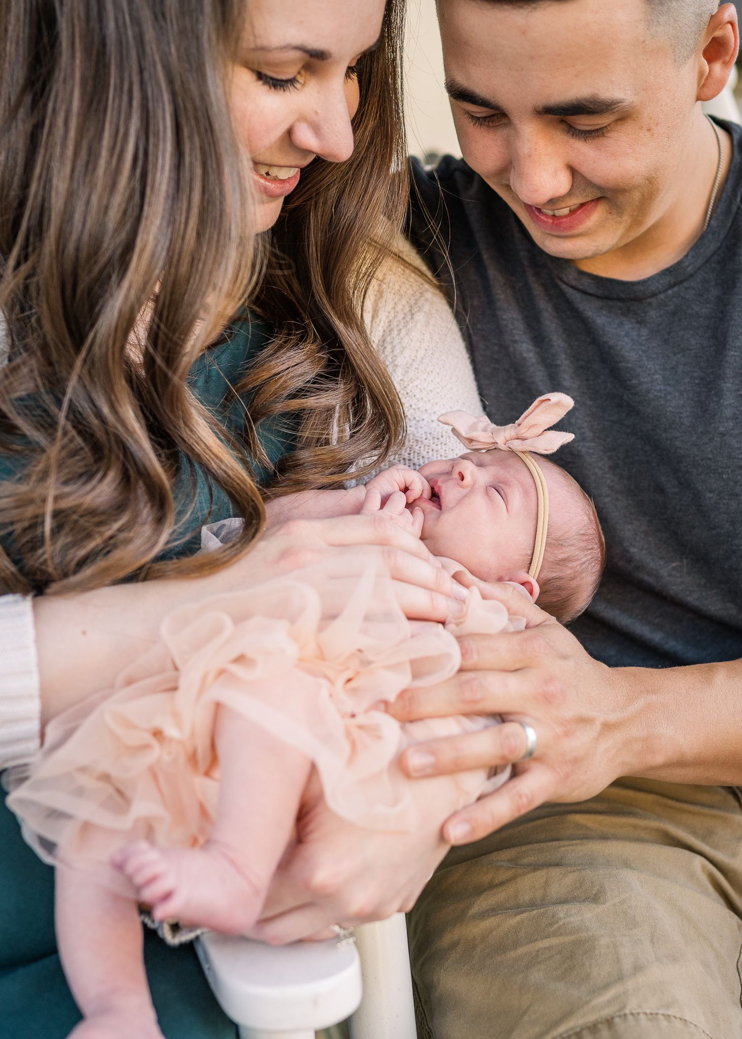 Parents sharing an intimate moment while holding their sleeping newborn in pink outfit.
