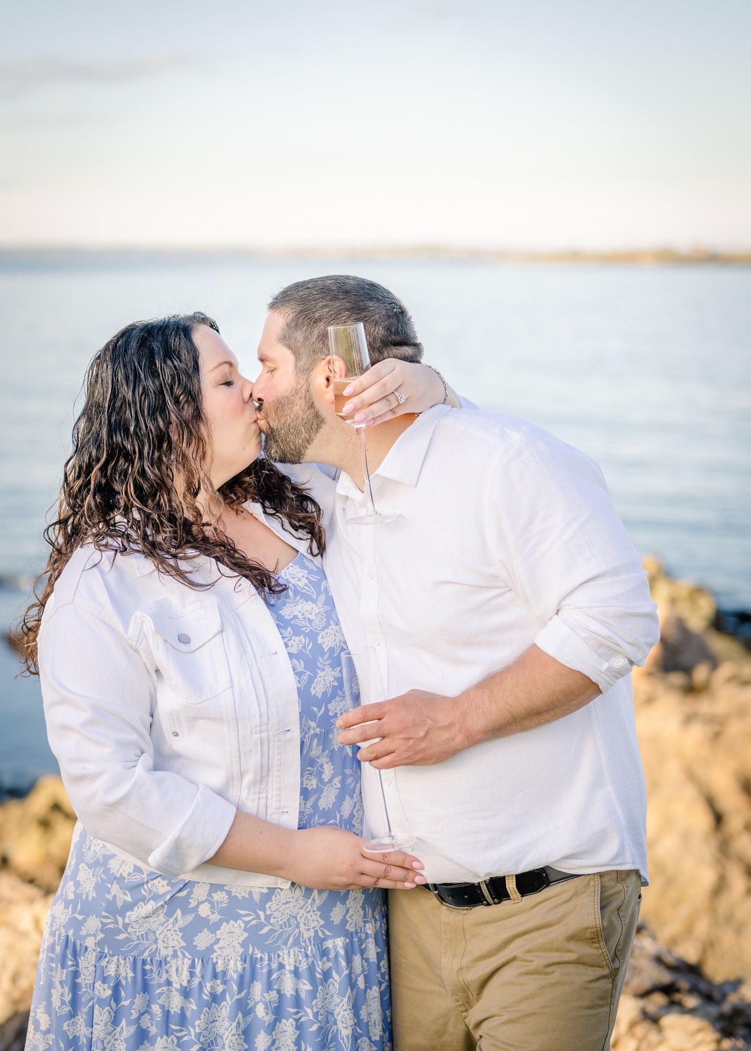 A romantic moment shared between a couple in white and blue outfits by the seaside.