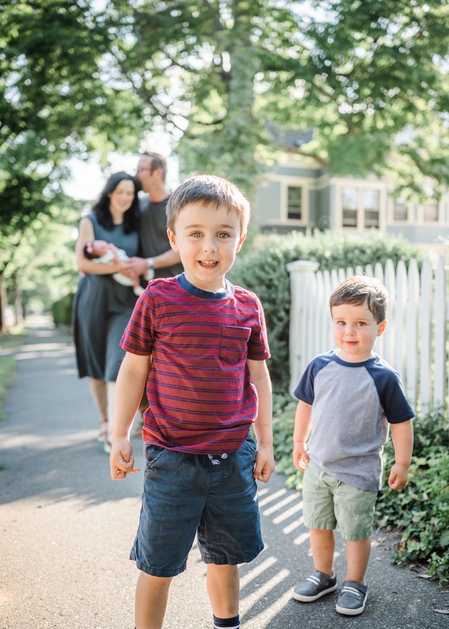 Children in casual summer clothes playing on sidewalk with trees and fence background.