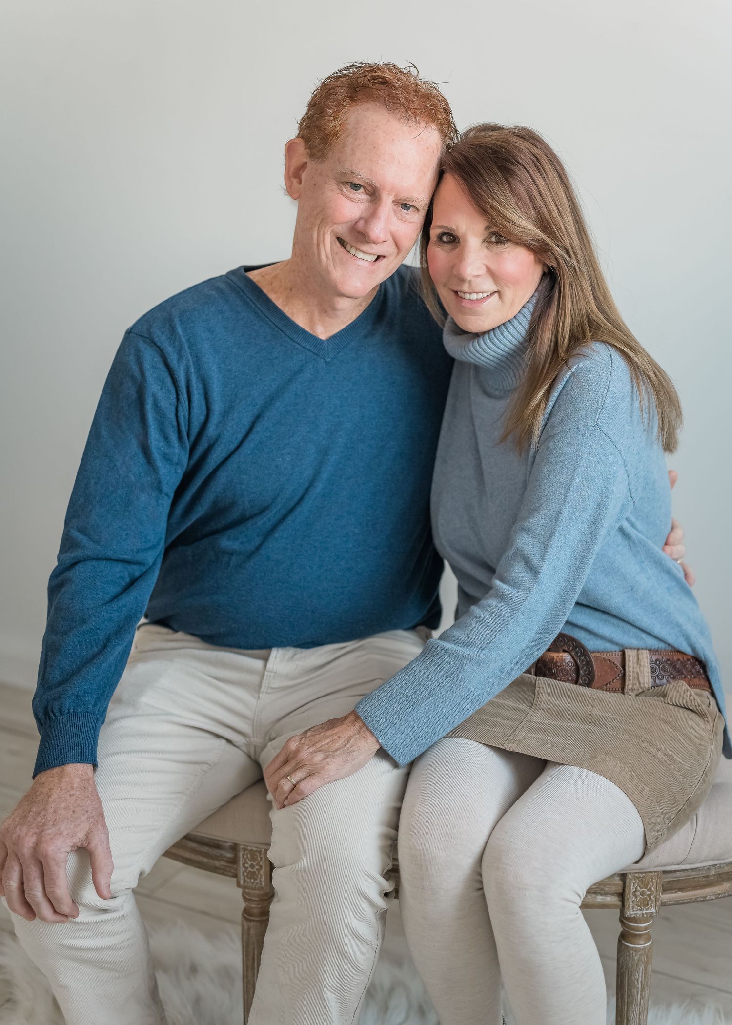 A couple in blue and gray sweaters share tender moments while sitting together on a light colored bench.