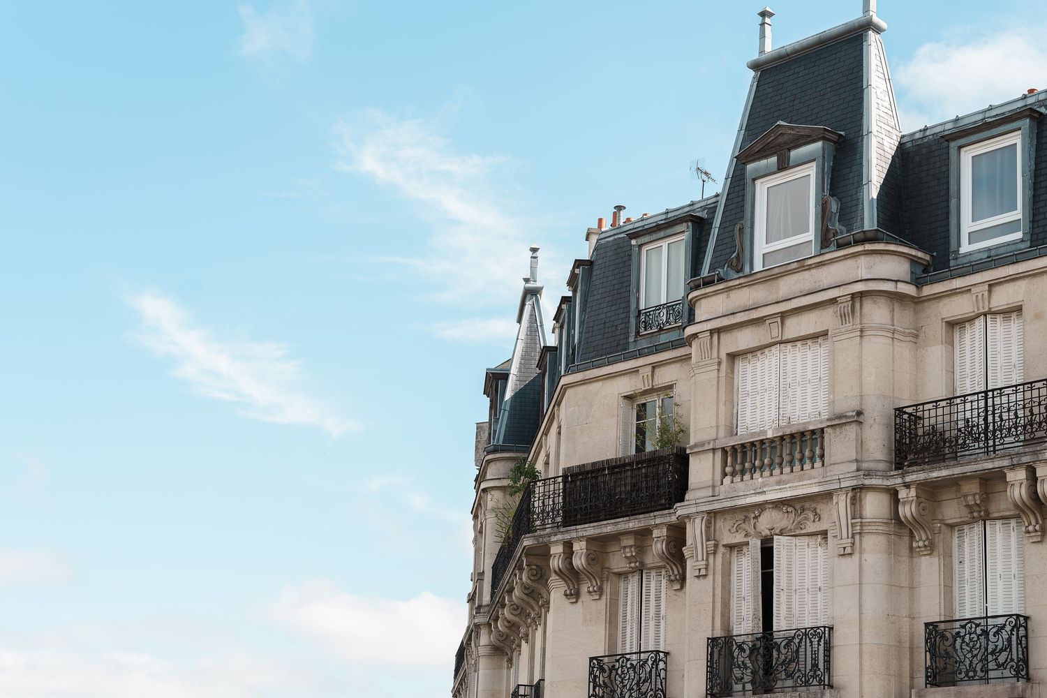 Classic Parisian apartment buildings with ornate balconies and mansard roofs line a street under blue skies.