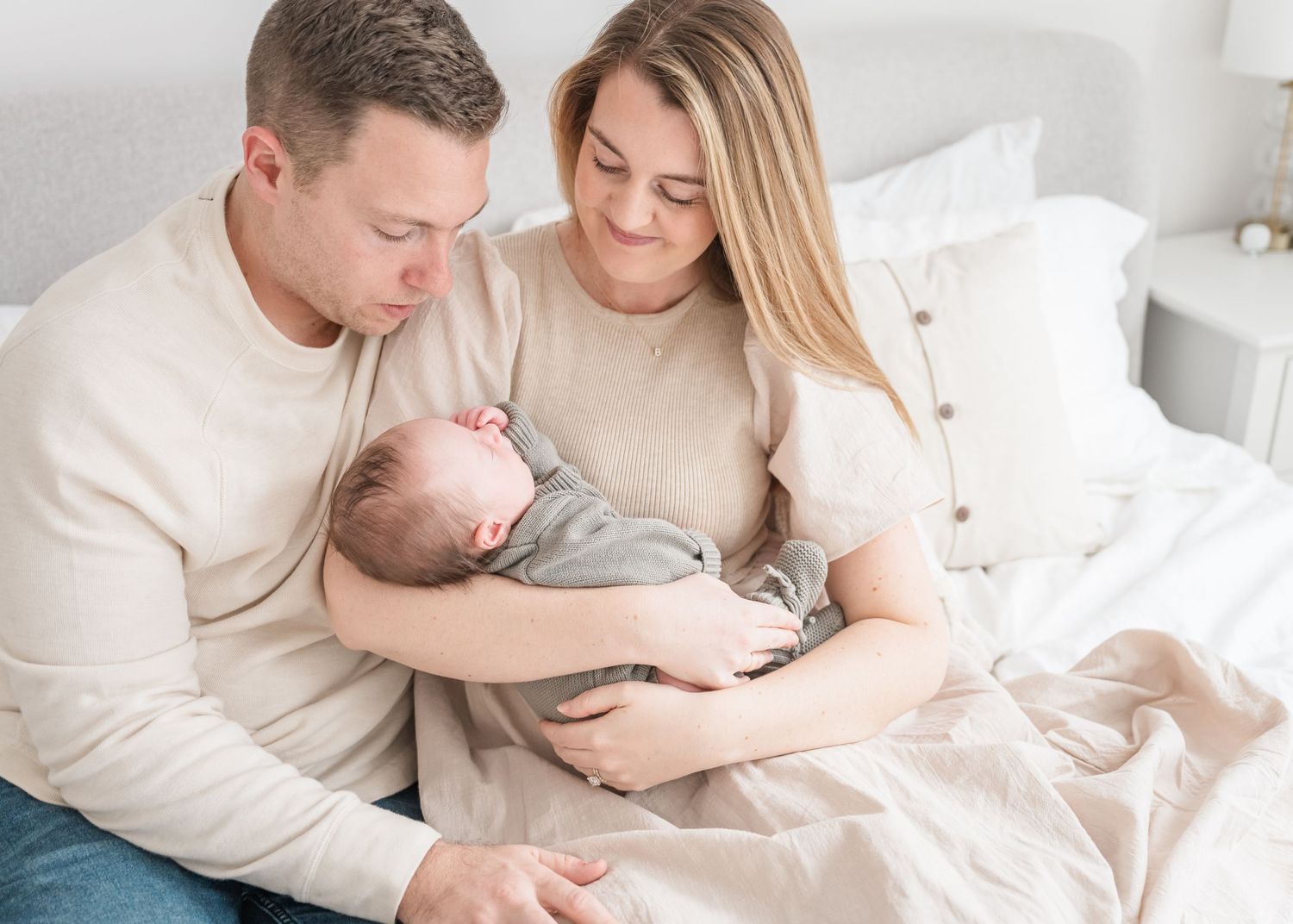 Intimate family moment in bed with newborn baby dressed in grey sleepwear.