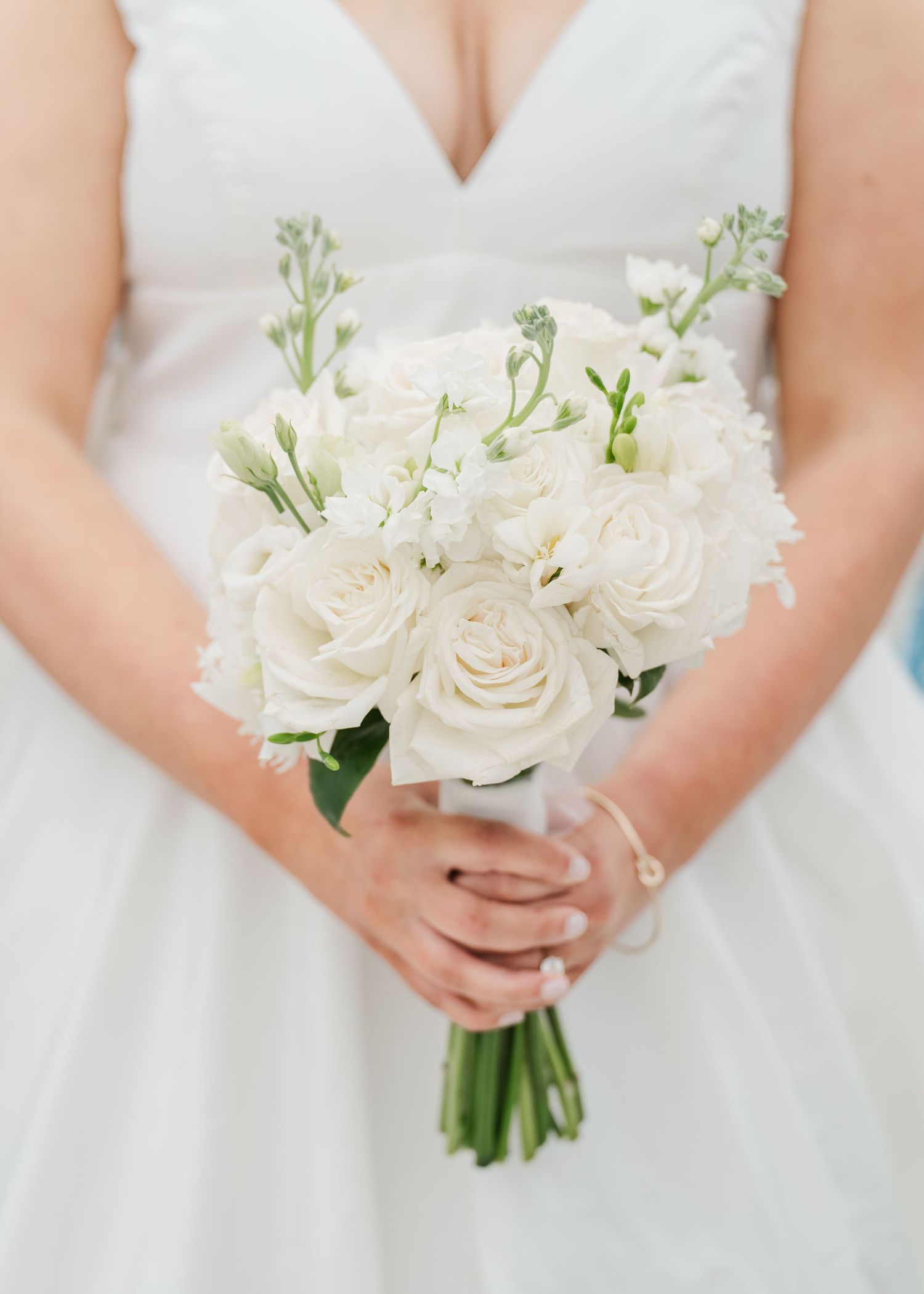 Elegant white rose and floral bouquet held against white dress fabric.