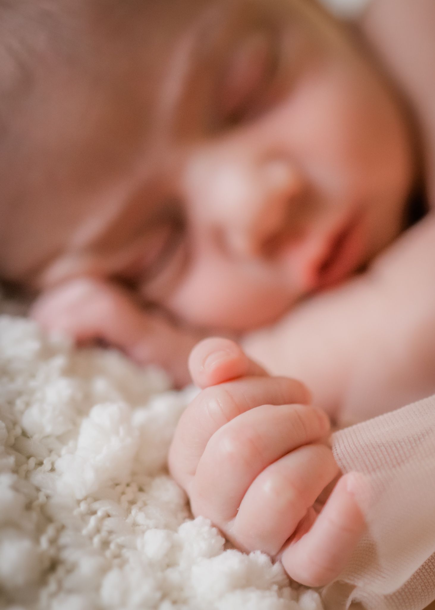 Close-up of a sleeping baby's tiny hand grasping soft fabric.