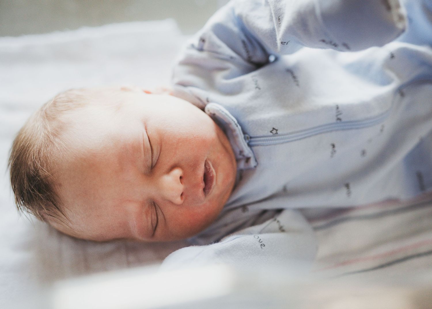 A sleeping newborn baby in a light blue outfit rests peacefully in a hospital bed.