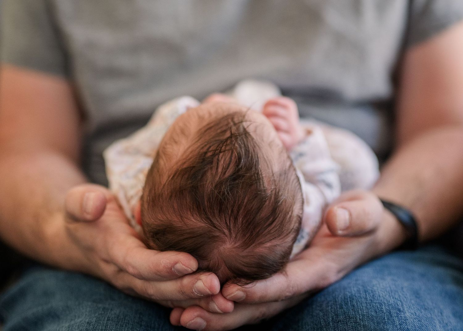 A sleeping newborn baby with dark hair rests gently in outstretched hands.