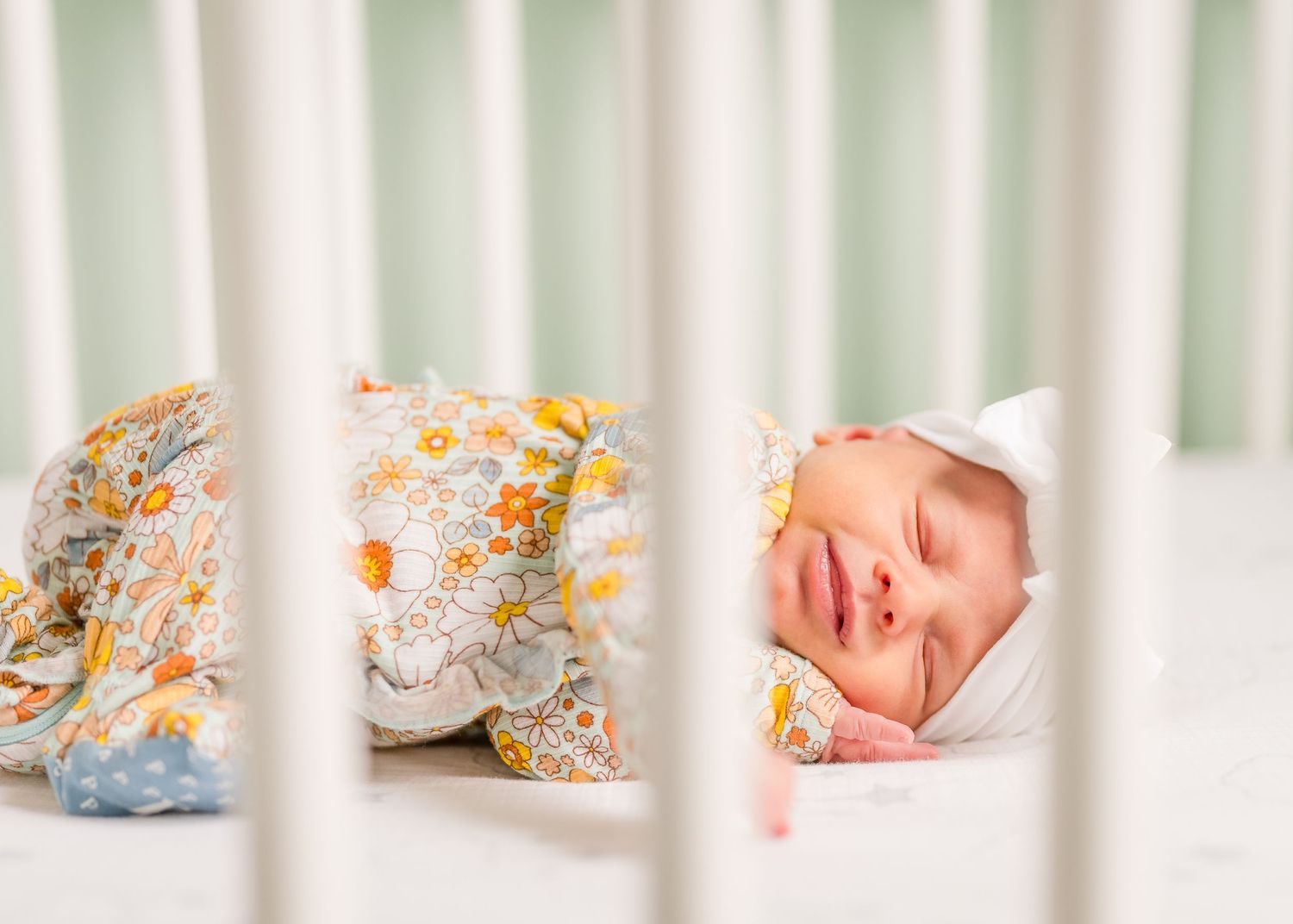 Peacefully sleeping newborn in white crib wearing floral print outfit.