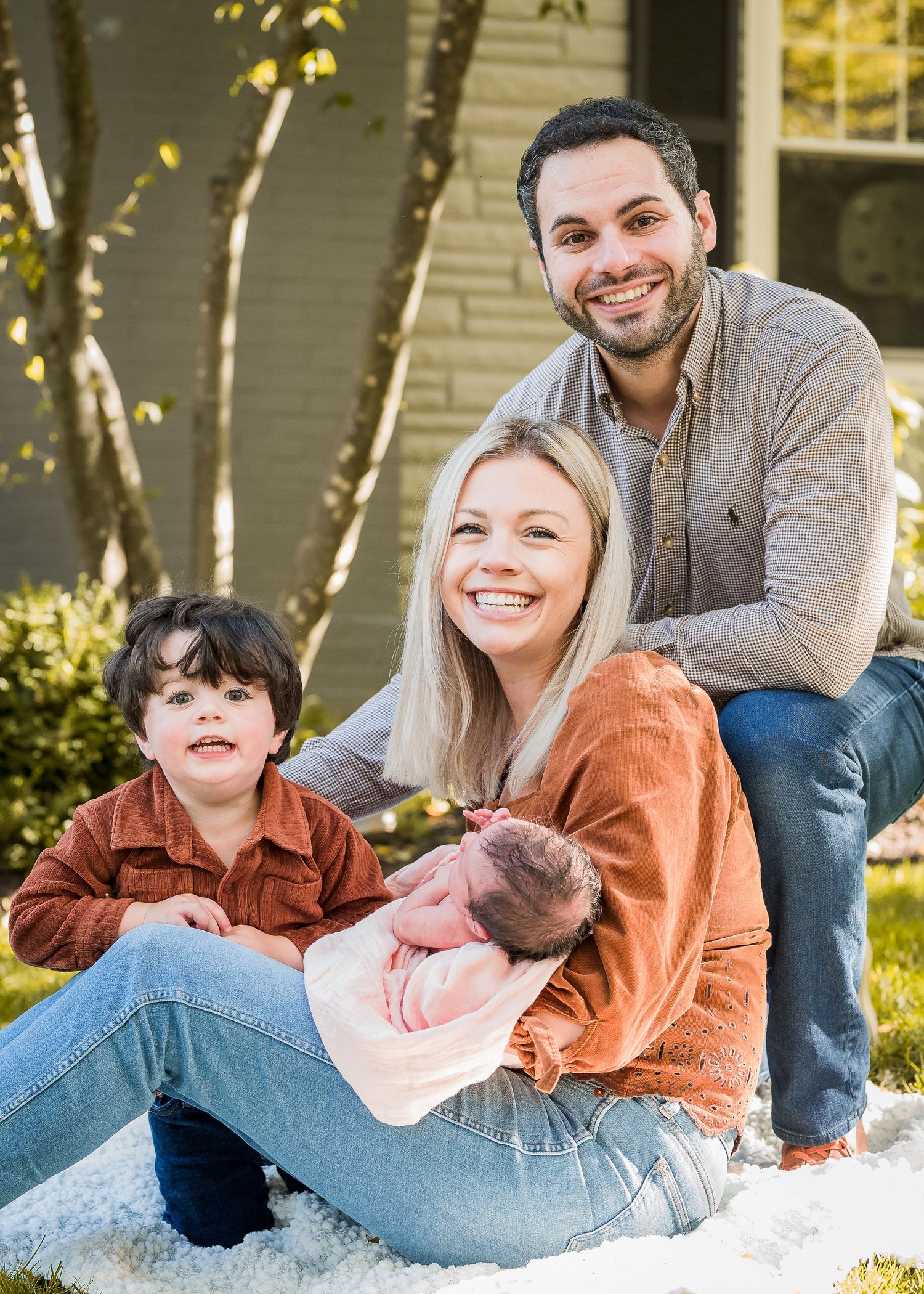Happy family of four sitting together outdoors on a white blanket.