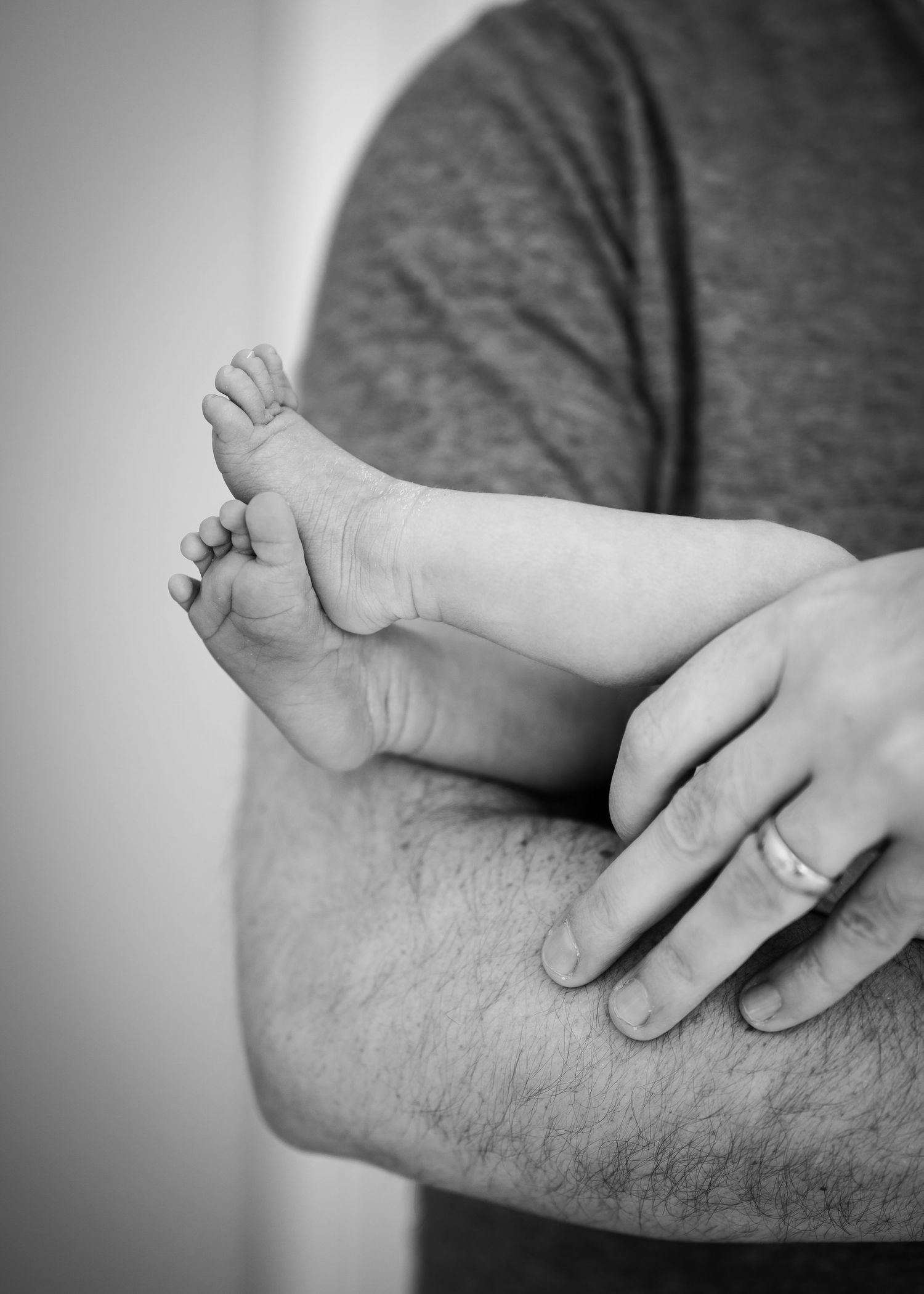 Black and white close-up of tiny baby foot being cradled against adult arm in tender moment.