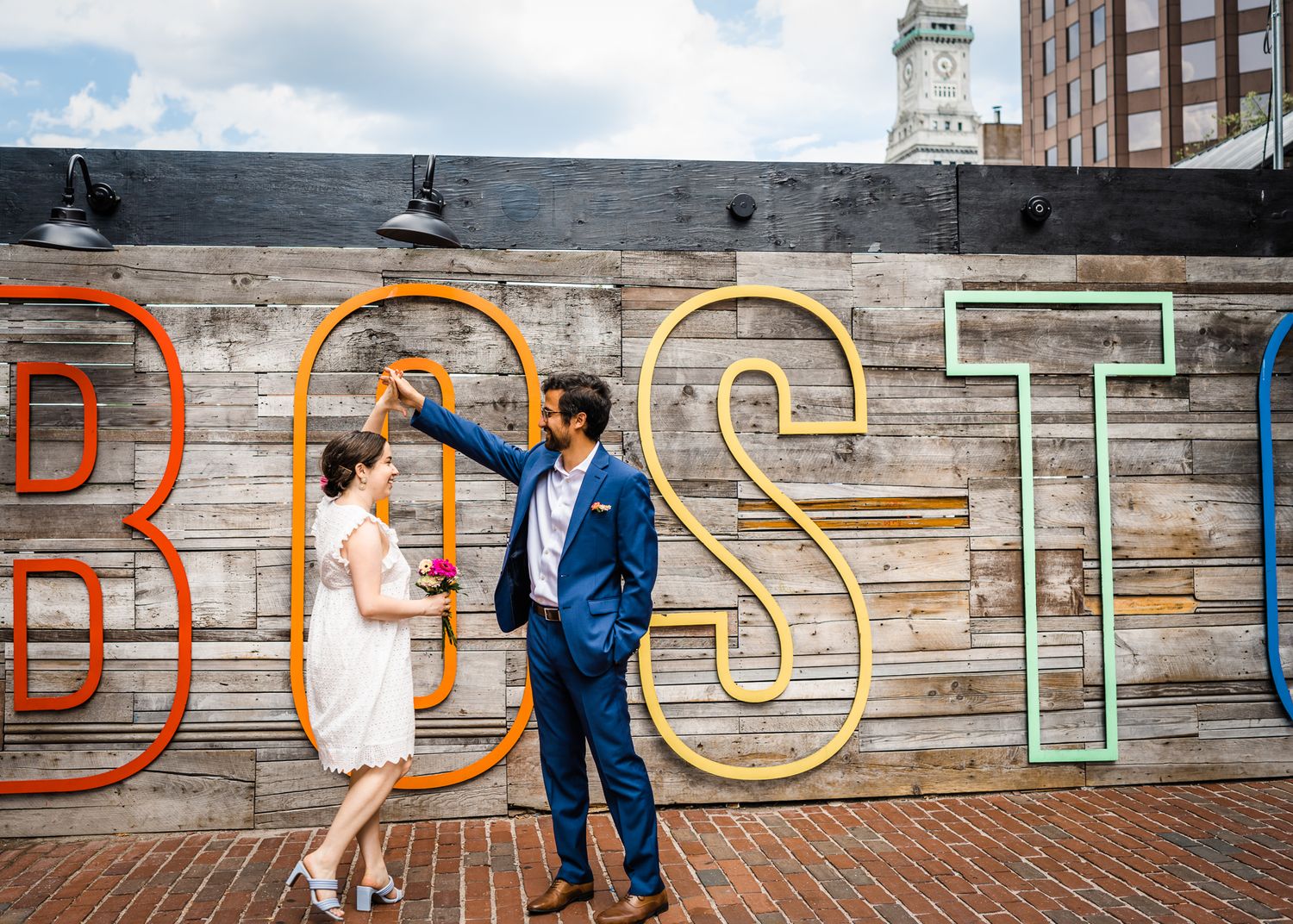 A couple poses in front of colorful 'BSTN' wall art on a rooftop deck.