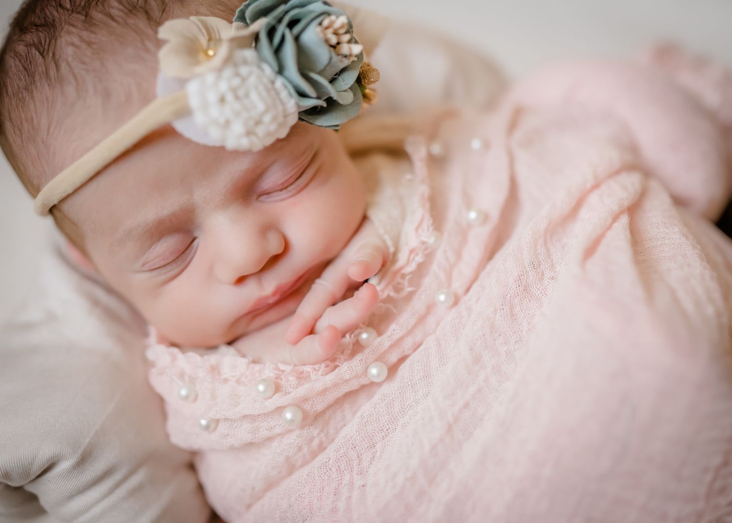 Sleeping baby wearing delicate lace dress and floral headband on white fabric.