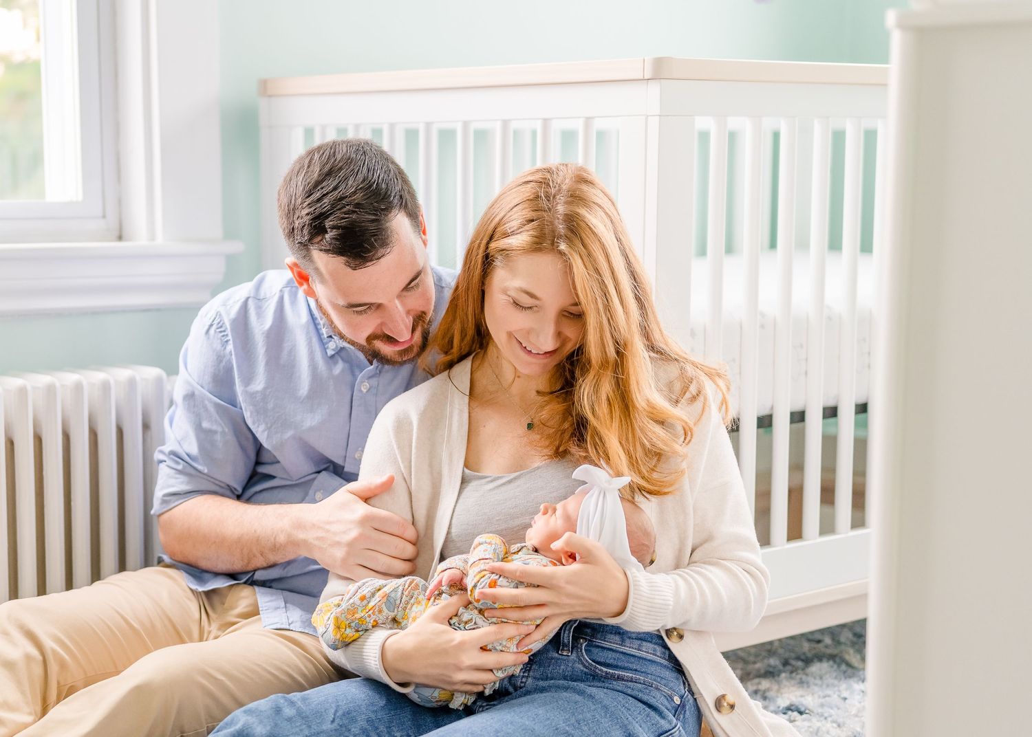Couple sitting in nursery with mint green walls holding newborn.