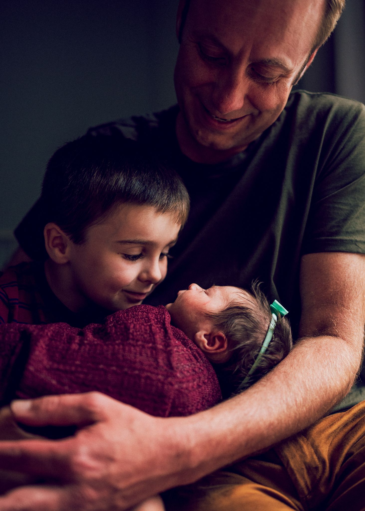 Family shares intimate moment together with newborn wearing green bow.