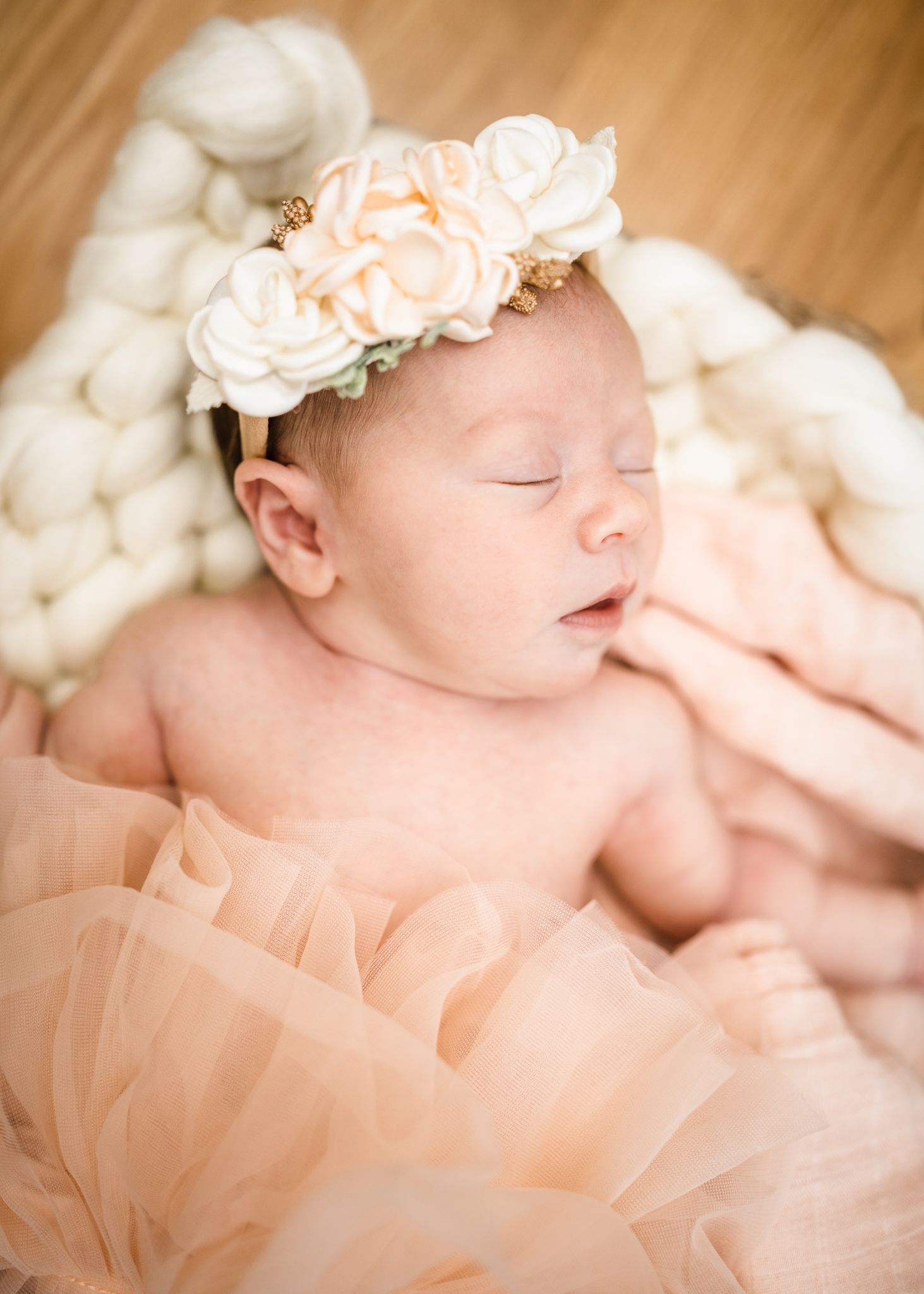 Sleeping baby wearing floral crown and peach tulle dress on white textured backdrop.