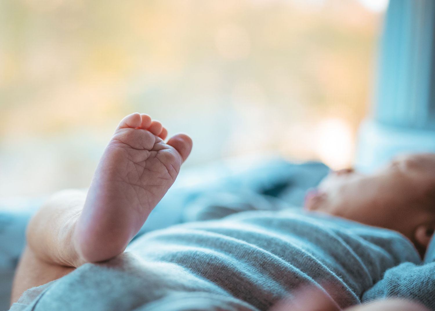 Close-up photo of a tiny baby foot against a soft blue background with gentle lighting.