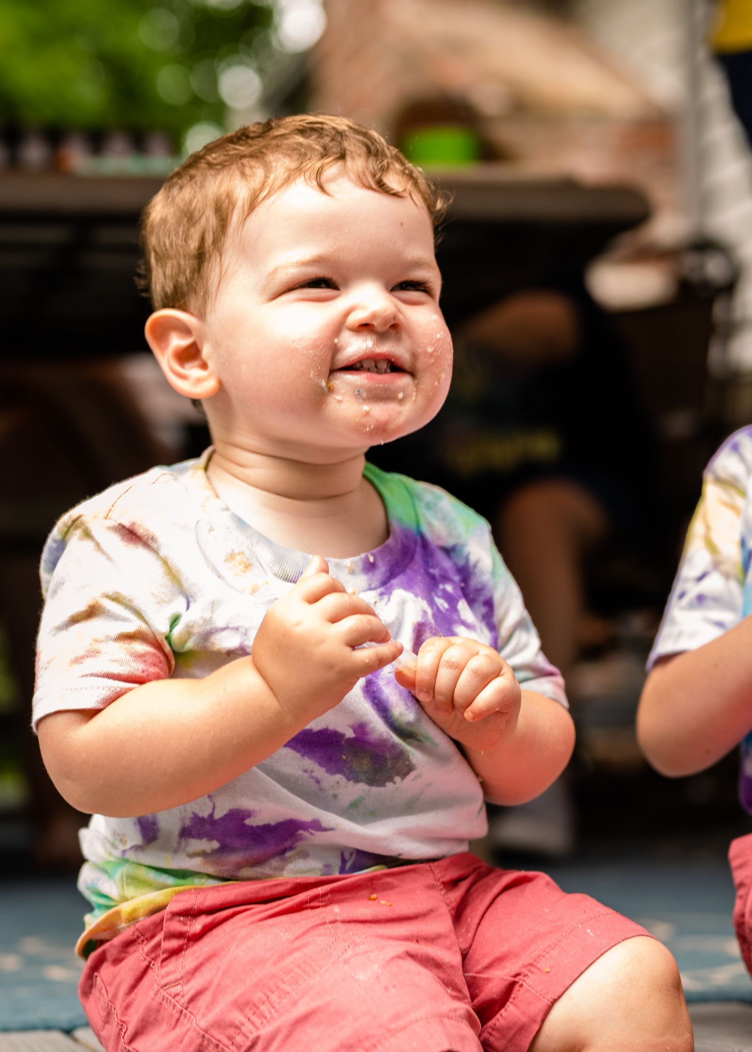 Child in tie-dye shirt laughing outdoors on sunny day.