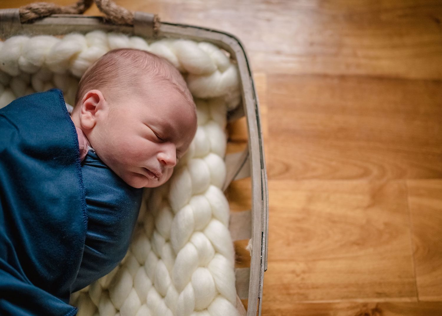 Sleeping baby in navy outfit resting on chunky knit blanket.