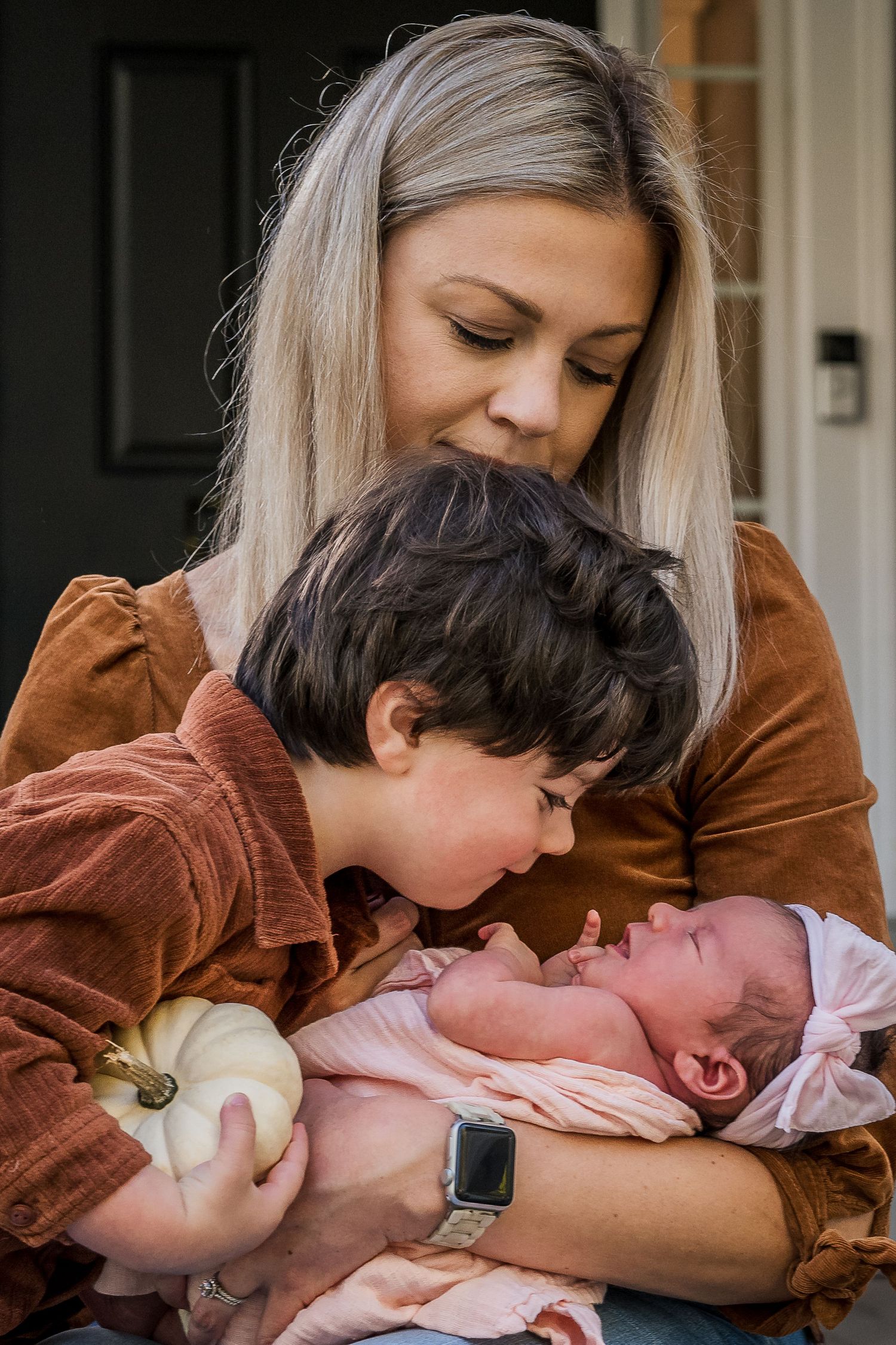 Family shares tender moment with newborn baby while holding white pumpkin.