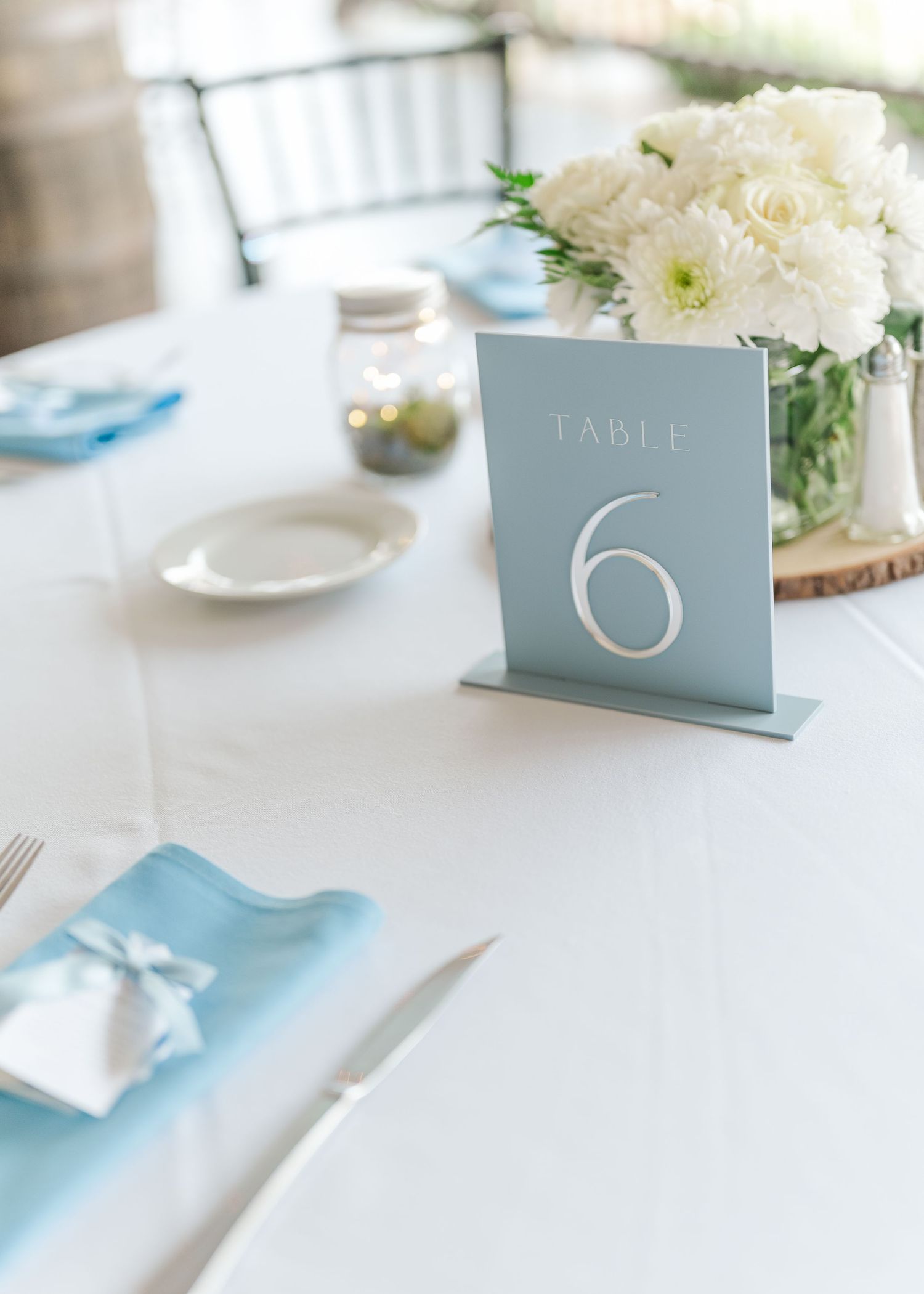 Elegant table settings with pale blue place cards and white floral centerpieces create a sophisticated wedding reception.