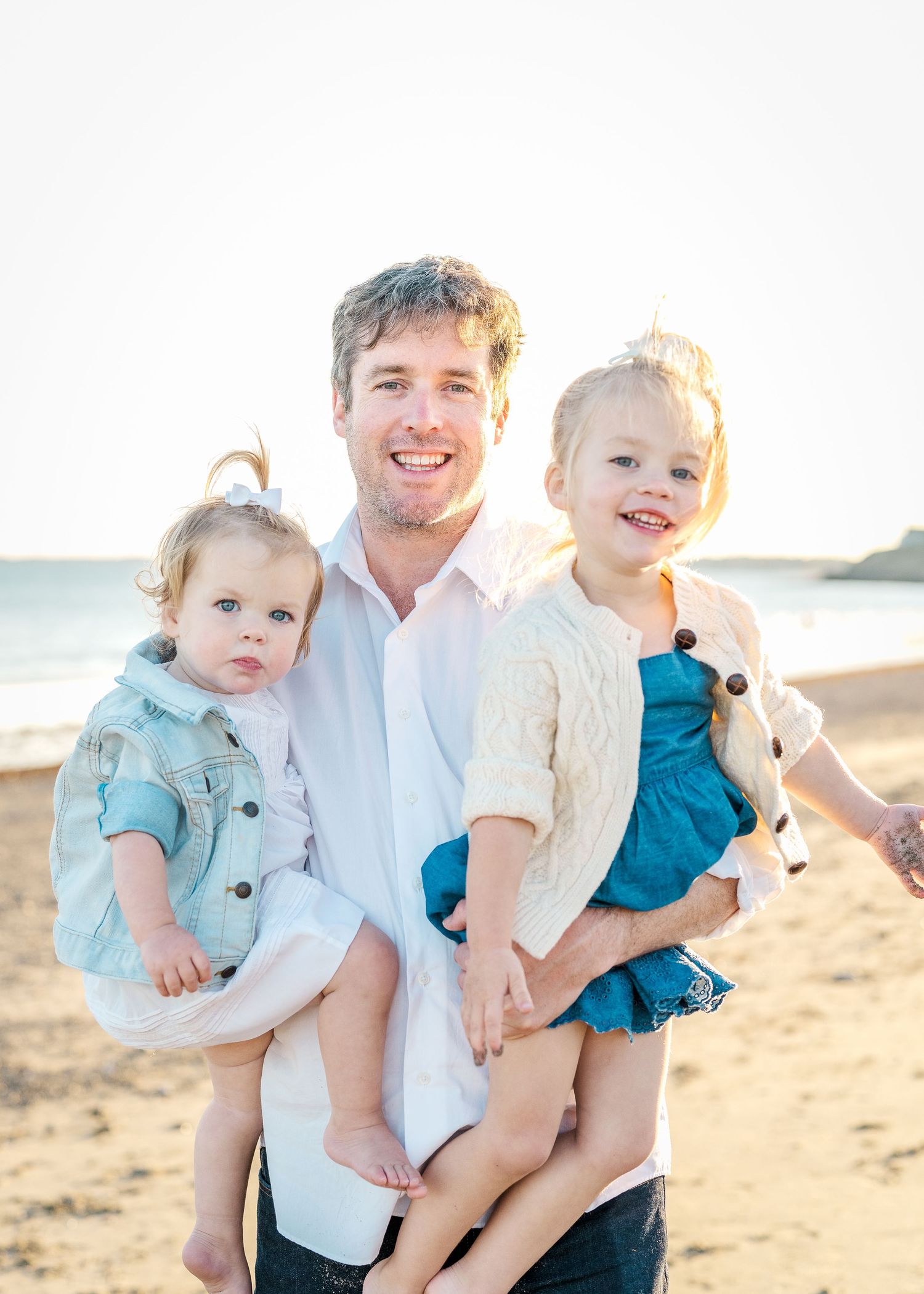 A joyful beach portrait featuring family members in casual attire standing together on golden sand at sunset.