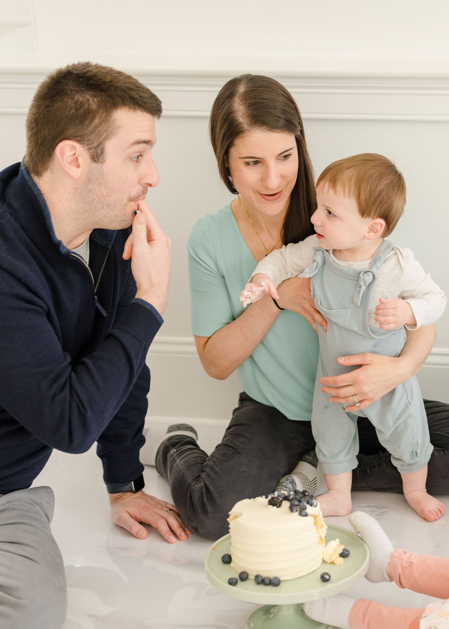 Family gathered around a white cake topped with blueberries on a plate during a celebration.