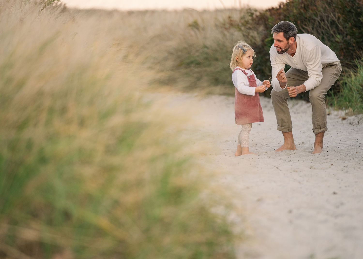 Family walking together along a sandy beach path during golden hour at sunset.
