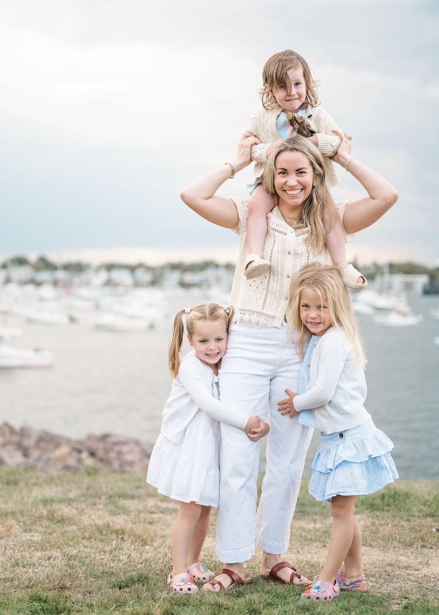A group in coordinating white and blue outfits crouches together on a coastal hillside with boats visible in the water.