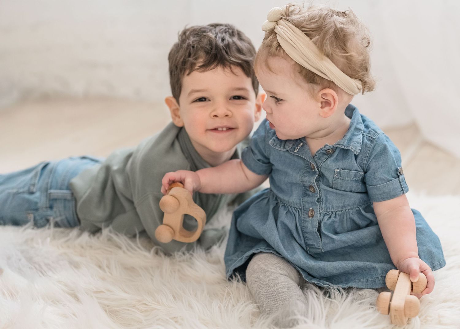 Two young children in casual outfits share a sweet moment while sitting together on a white furry rug.