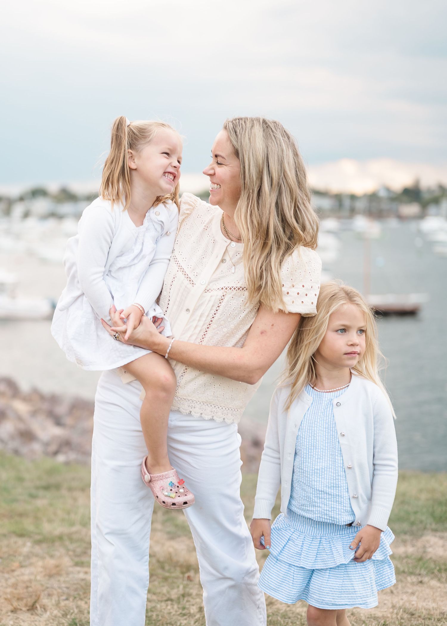 A family dressed in white and blue outfits poses together near a marina on a sunny day.