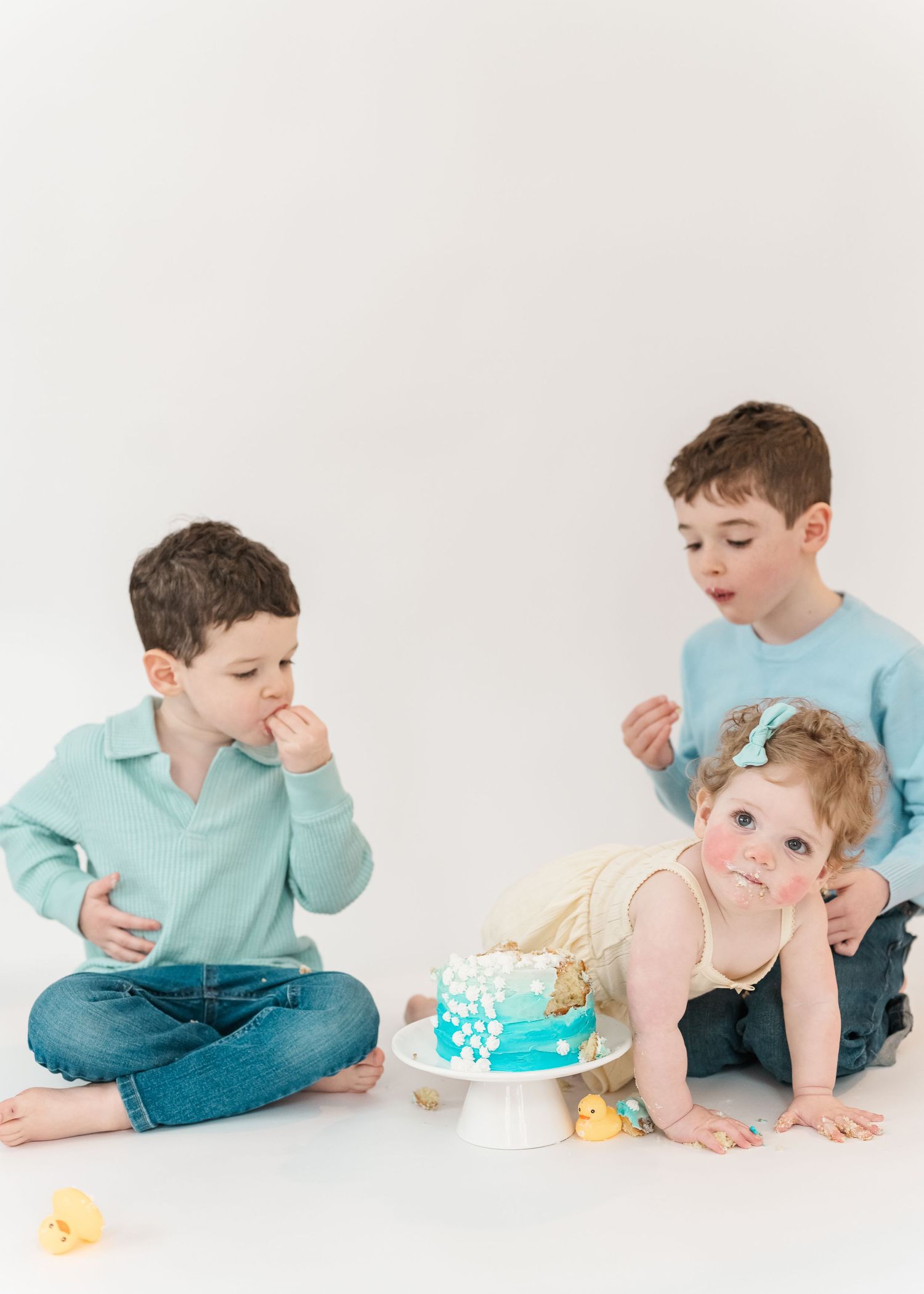 Cake smash. Three children sit on the floor during a cake smash photo session with a turquoise decorated cake.